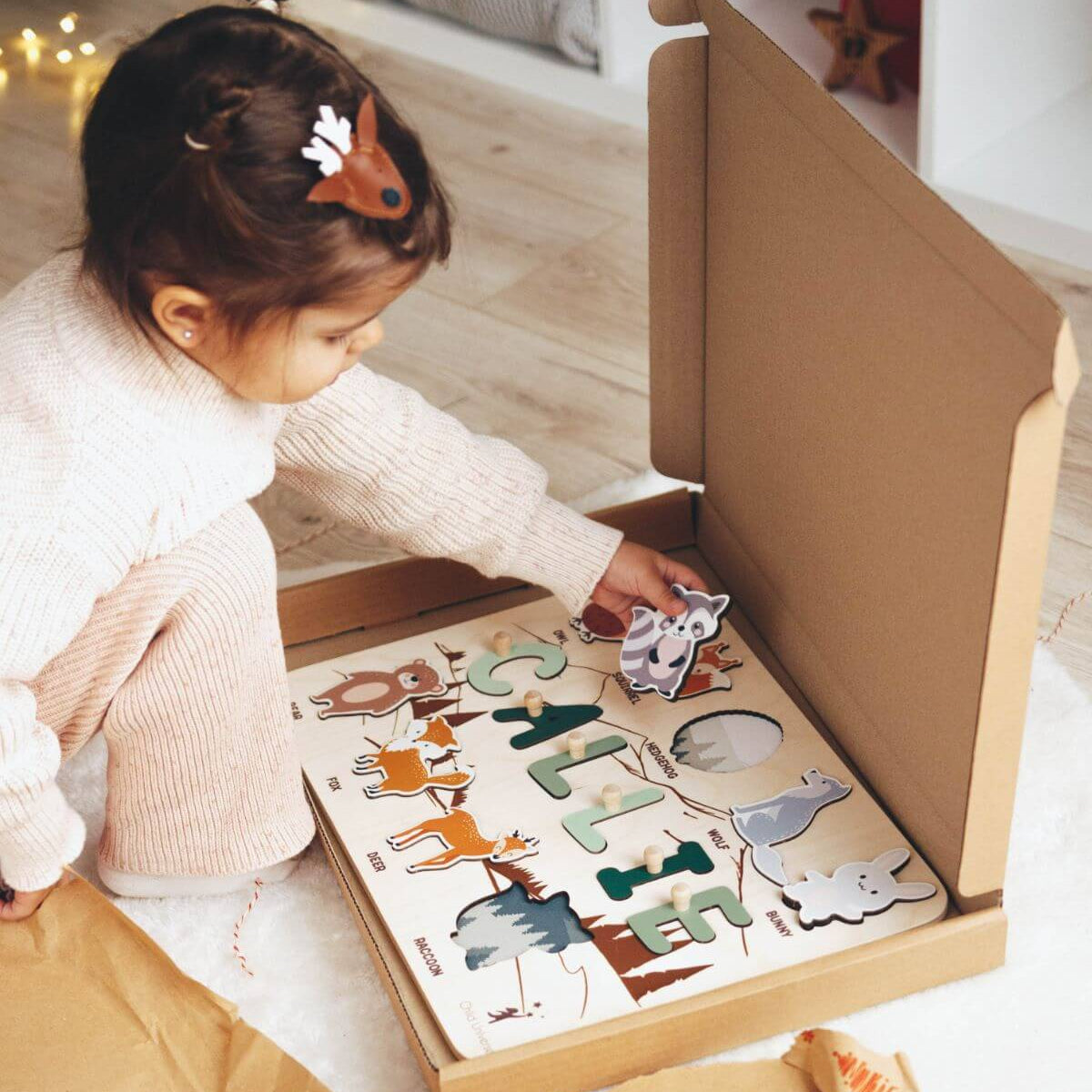Child playing with a puzzle in a cardboard box on a wooden floor.