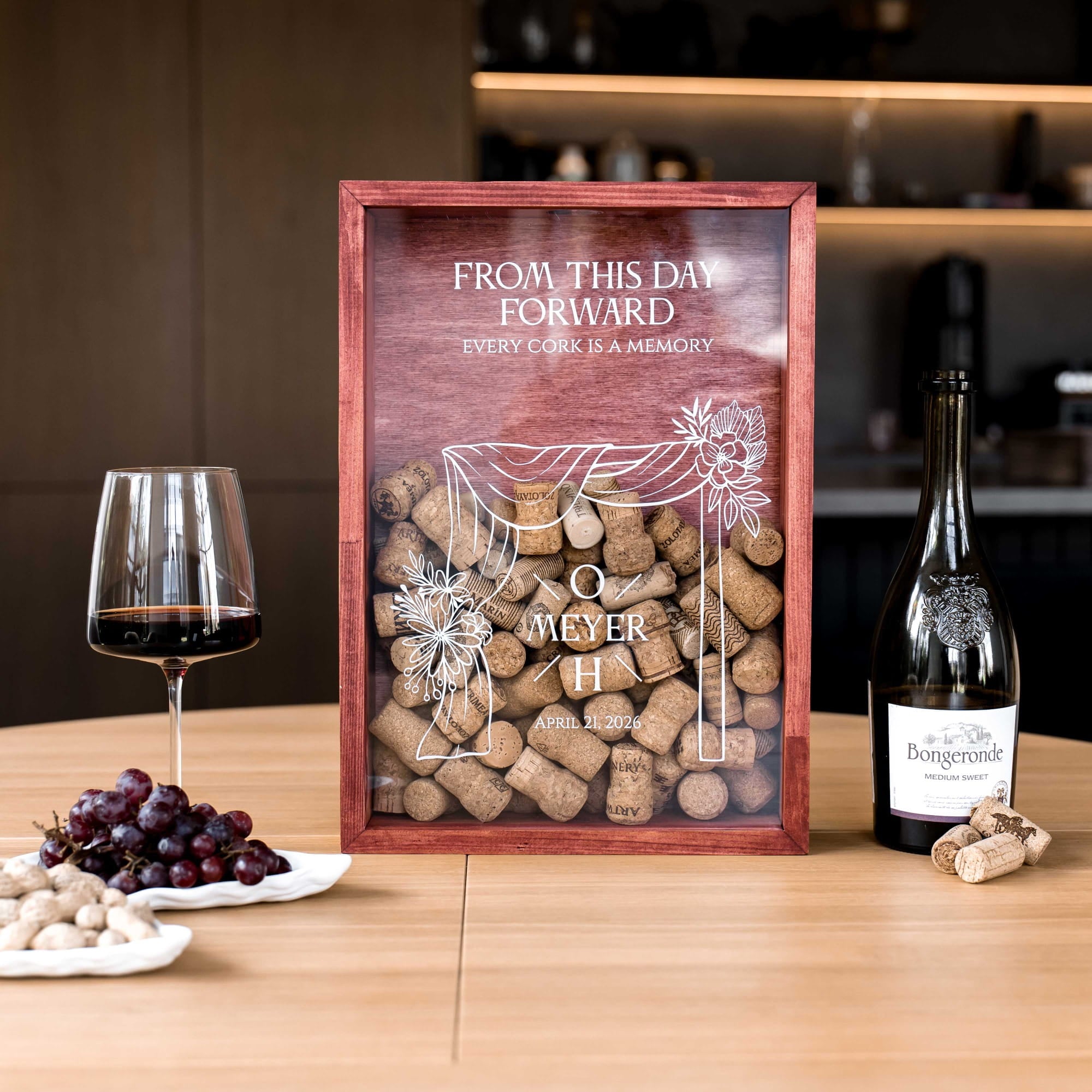 A personalized wooden wine cork box with a glass front panel sits on a wooden table