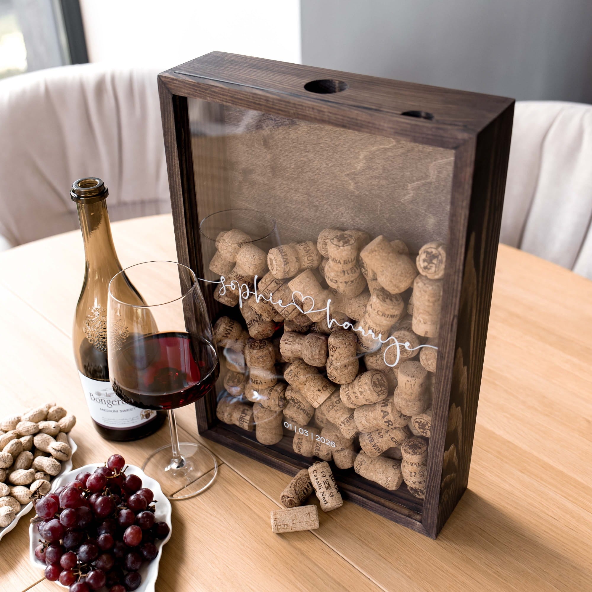 A dark wood wine cork display box with a clear front panel sits on a wooden table