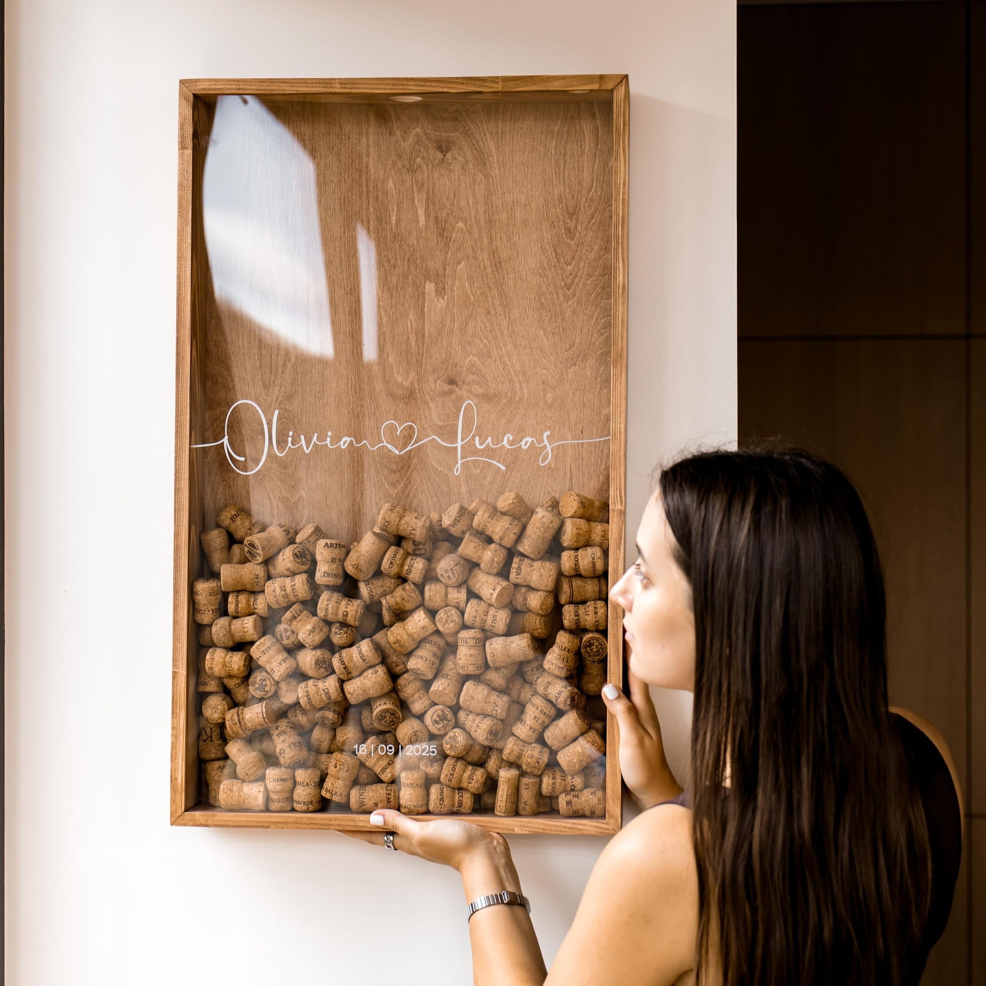 A woman holds a large wooden framed wall display filled with wine corks