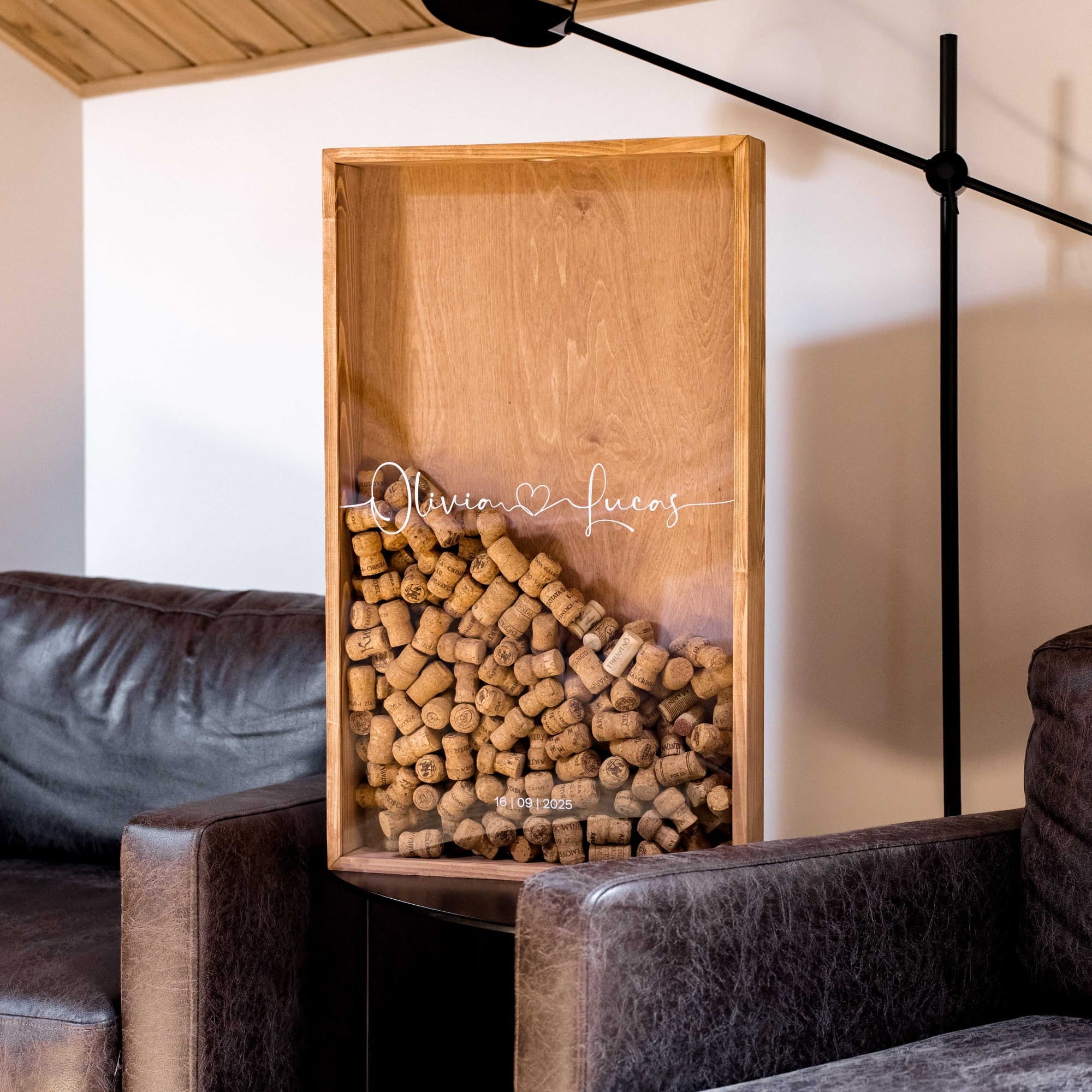 A rectangular wooden display box filled with wine corks, placed between two dark leather armchairs in a modern living room.