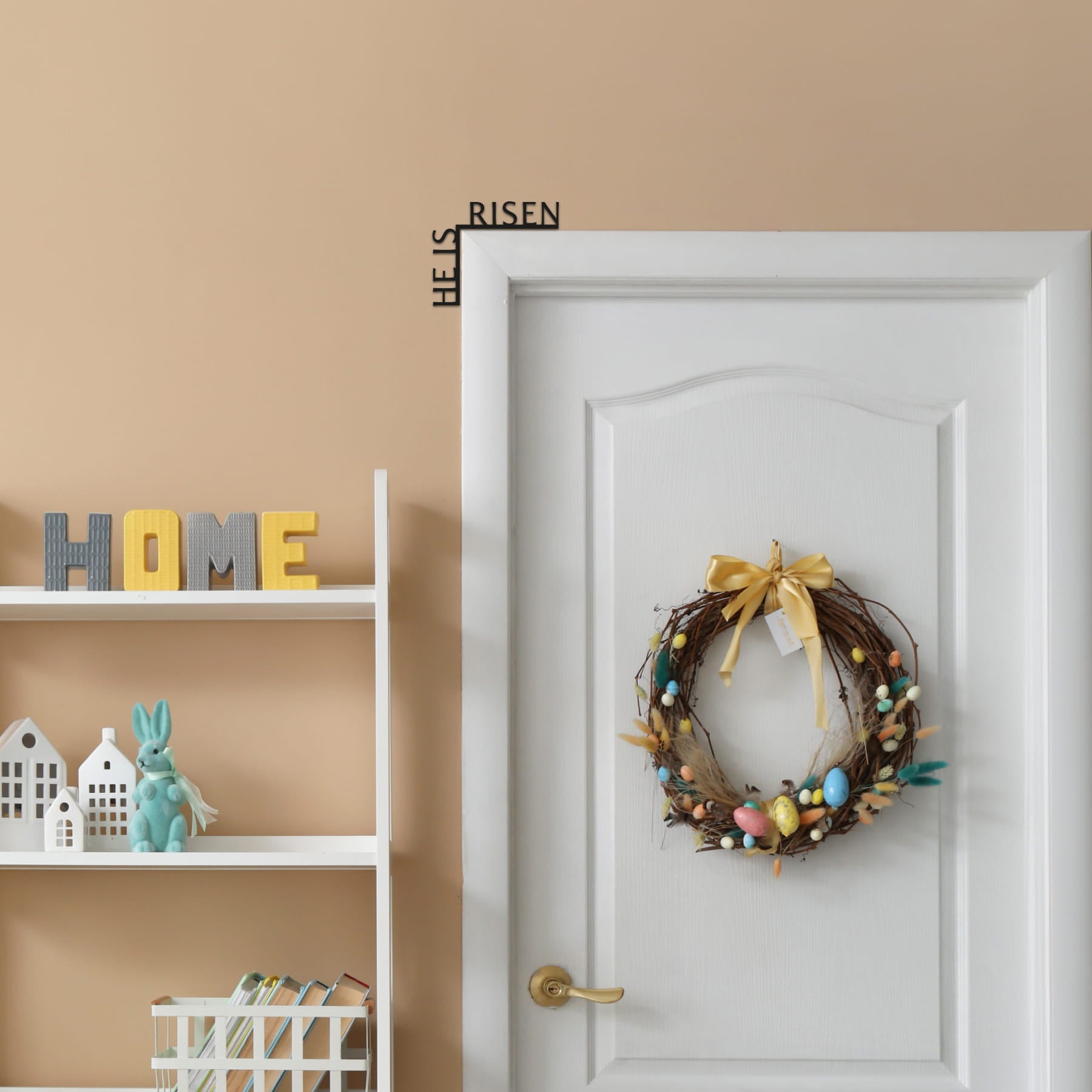 Decorative wreath with colorful eggs on a white door, 'HOME' sign on a shelf, and 'HELPS RISEN' wall art.