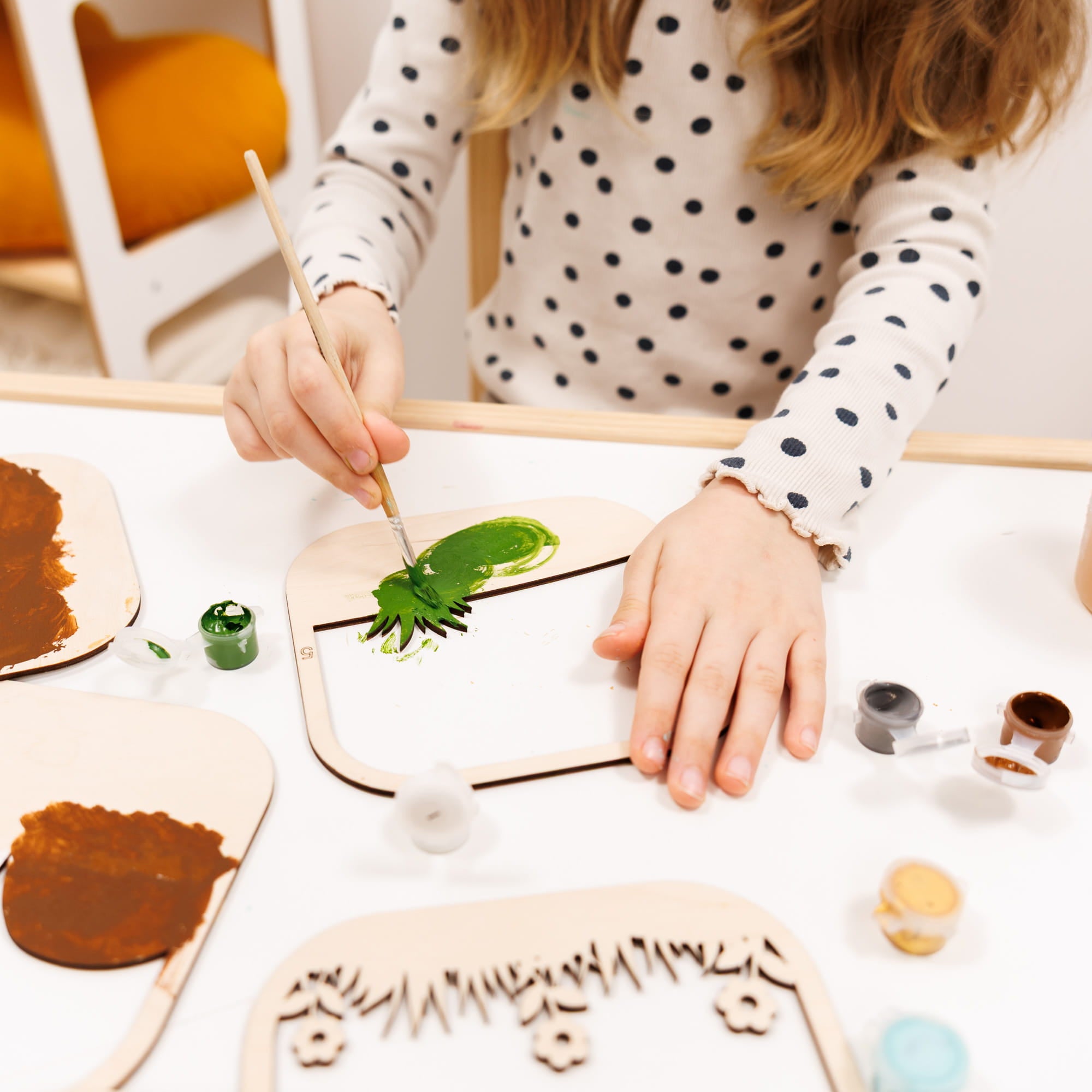 Child painting a wooden leaf craft with green paint