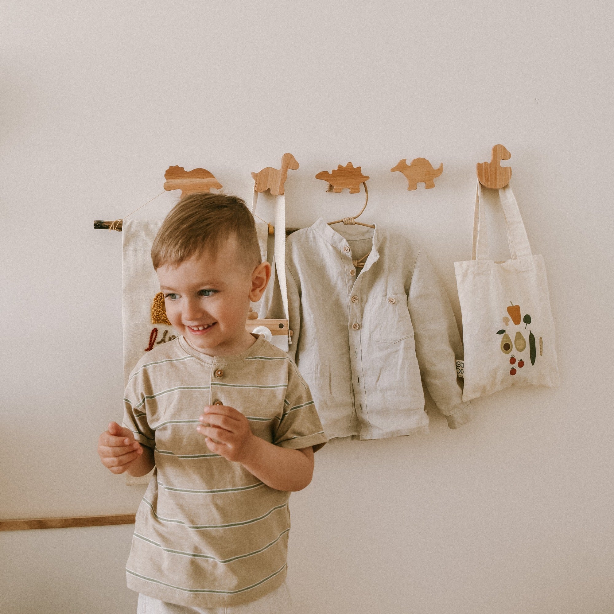Child standing in front of a wall with hanging clothes and a bag