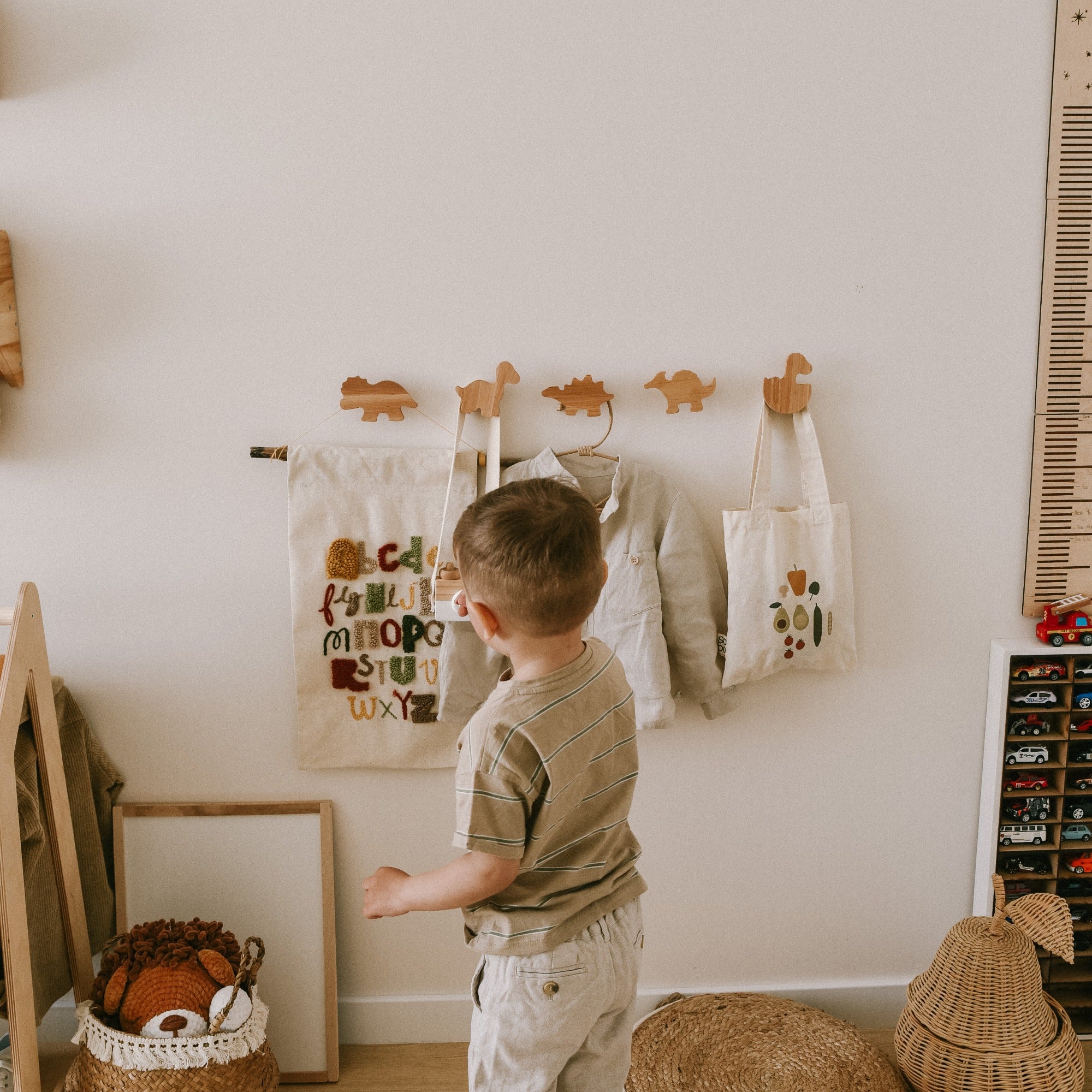 Child standing in a room with a coat rack and hanging bags.