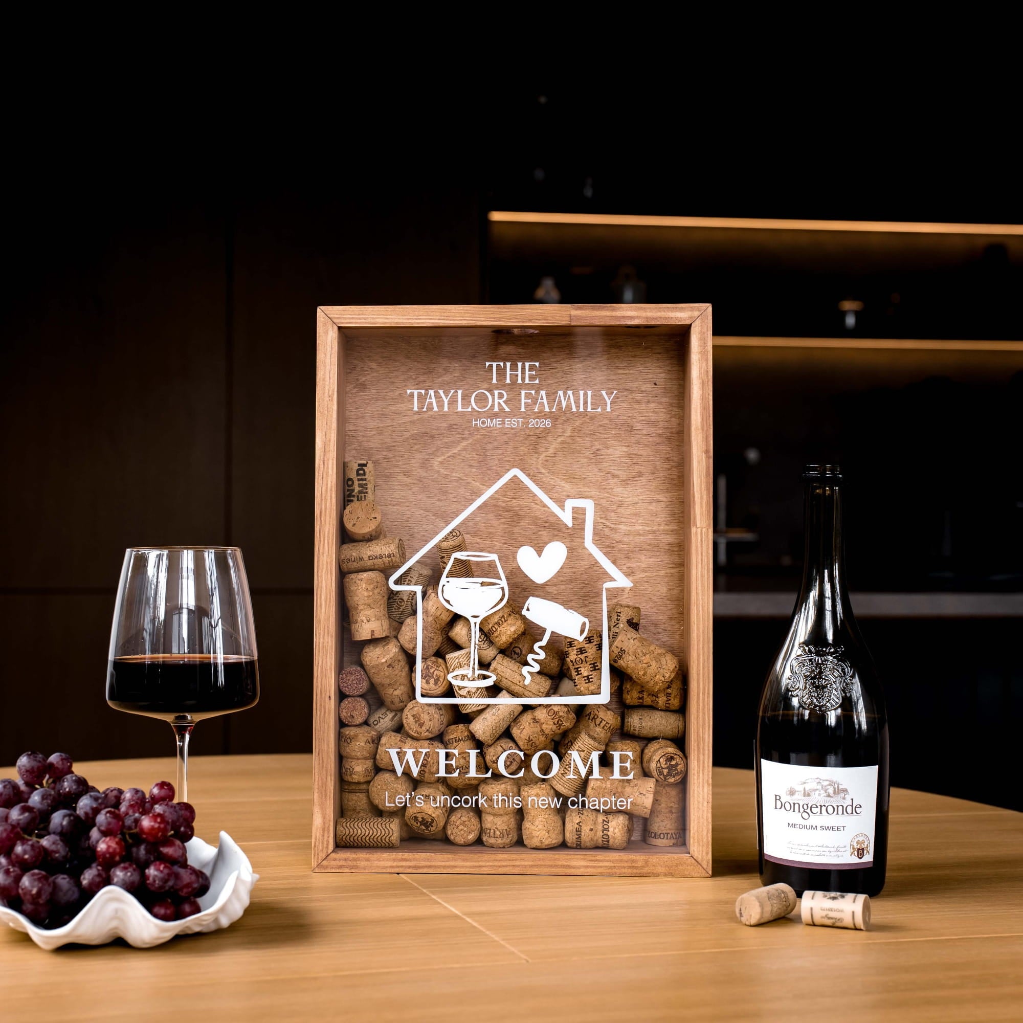 A personalized wooden wine tray displayed on a wooden table, flanked by a glass of red wine, a bowl of grapes, and a bottle of Burgundy wine.