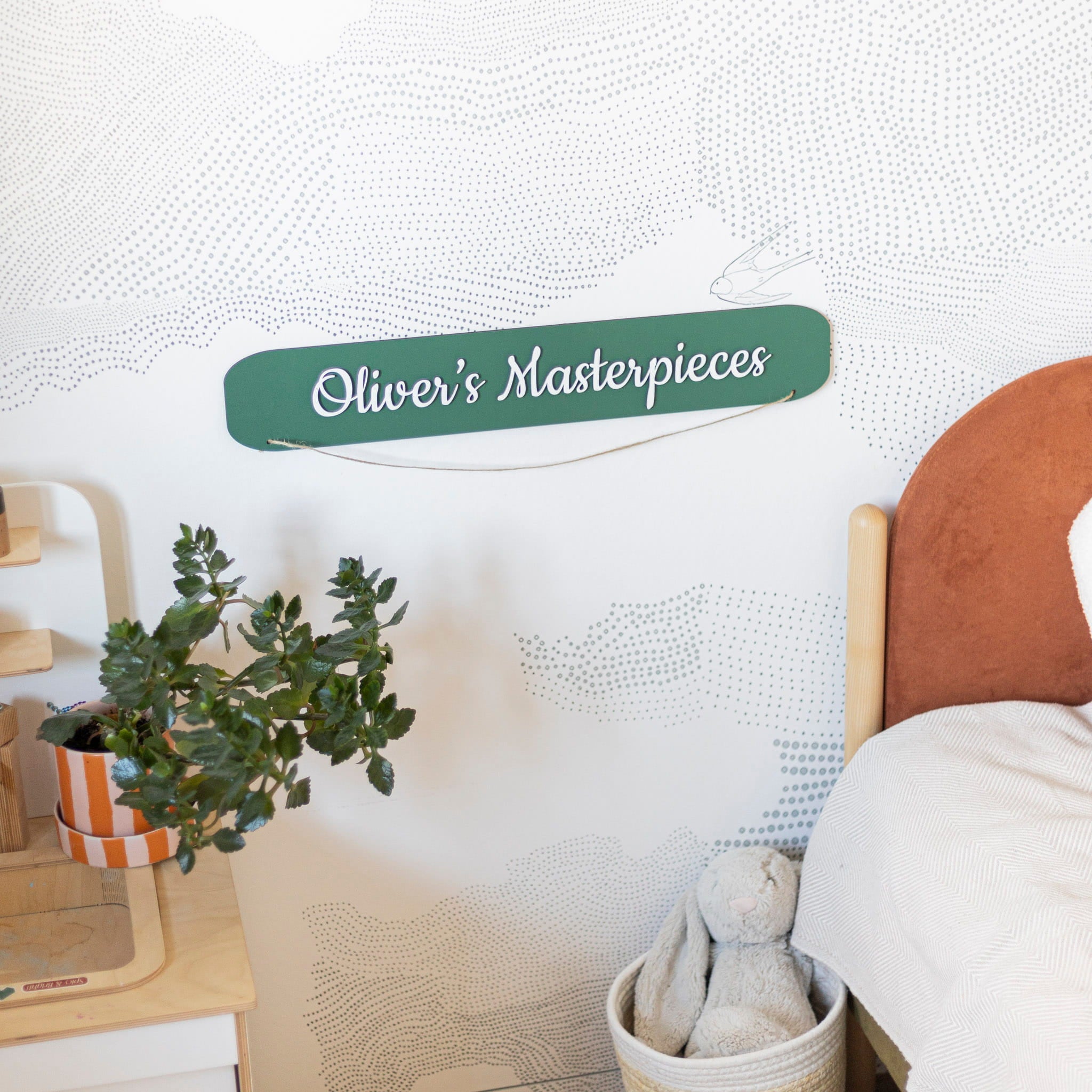 Children's room with a sign reading 'Oliver's Masterpieces' on a textured white wall.