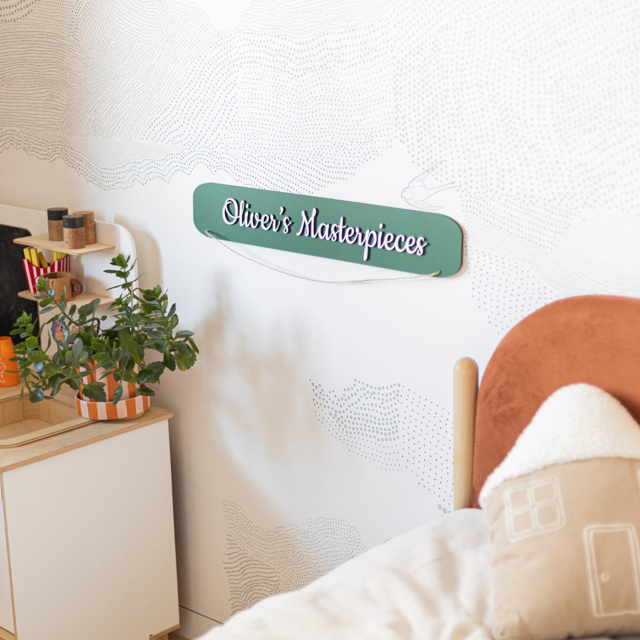 Decorative sign with 'Oliver's Masterpieces' on a wall above a bed.