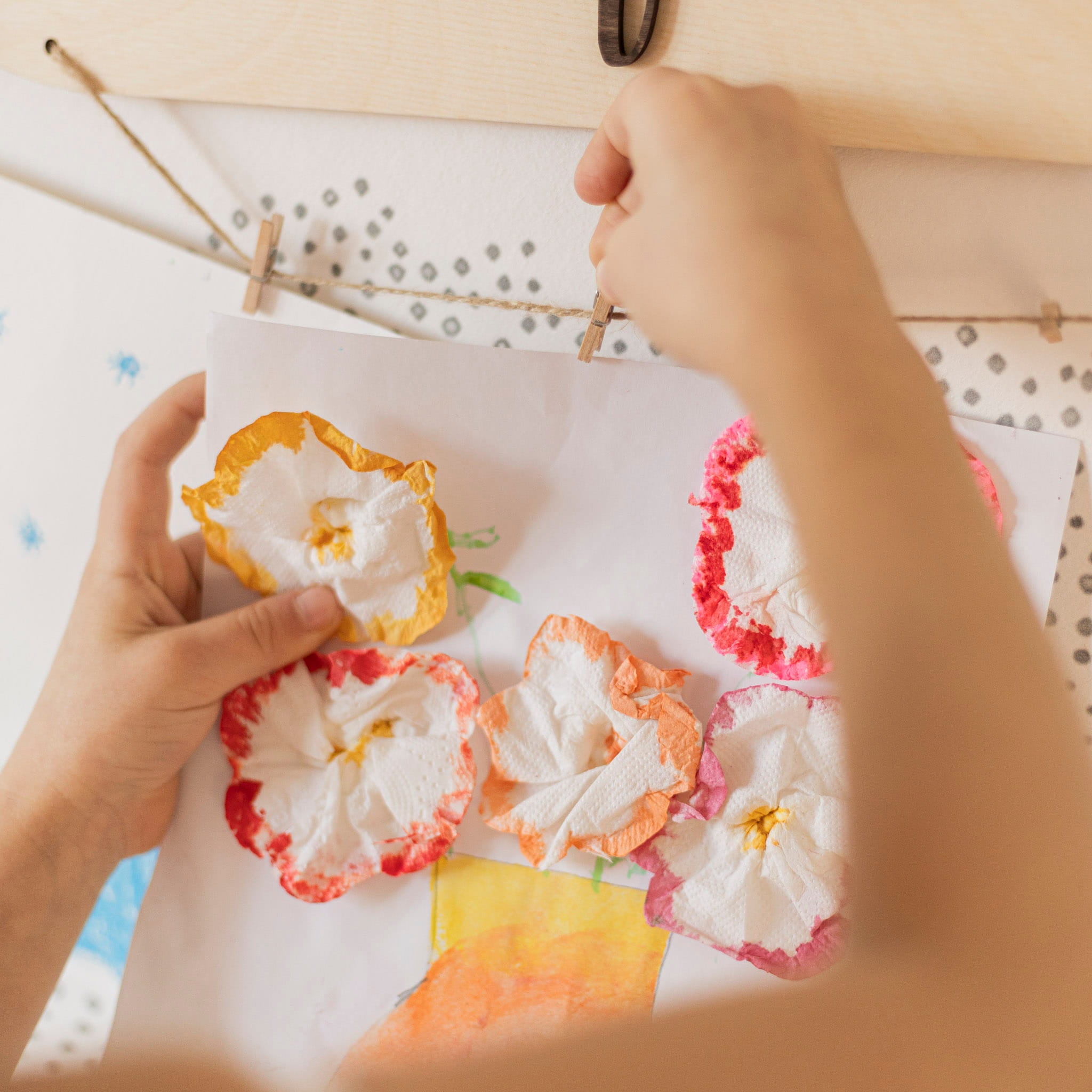 Colorful paper flowers on a white sheet with hands holding one flower.