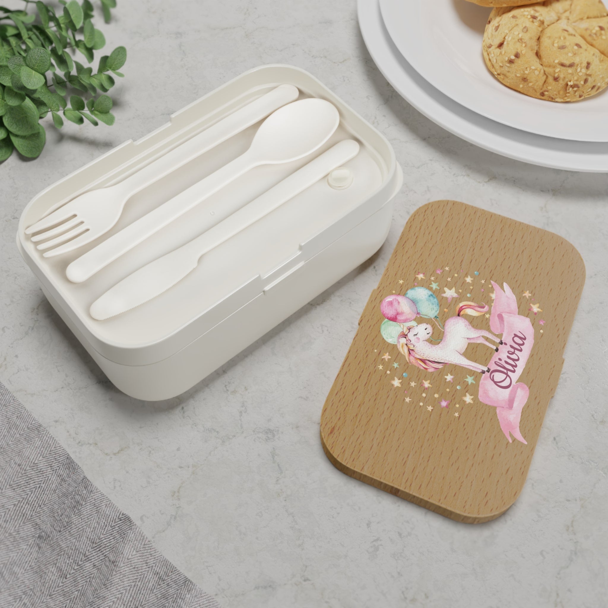 White cutlery set in a container with a wooden lid featuring a unicorn design on a gray surface.