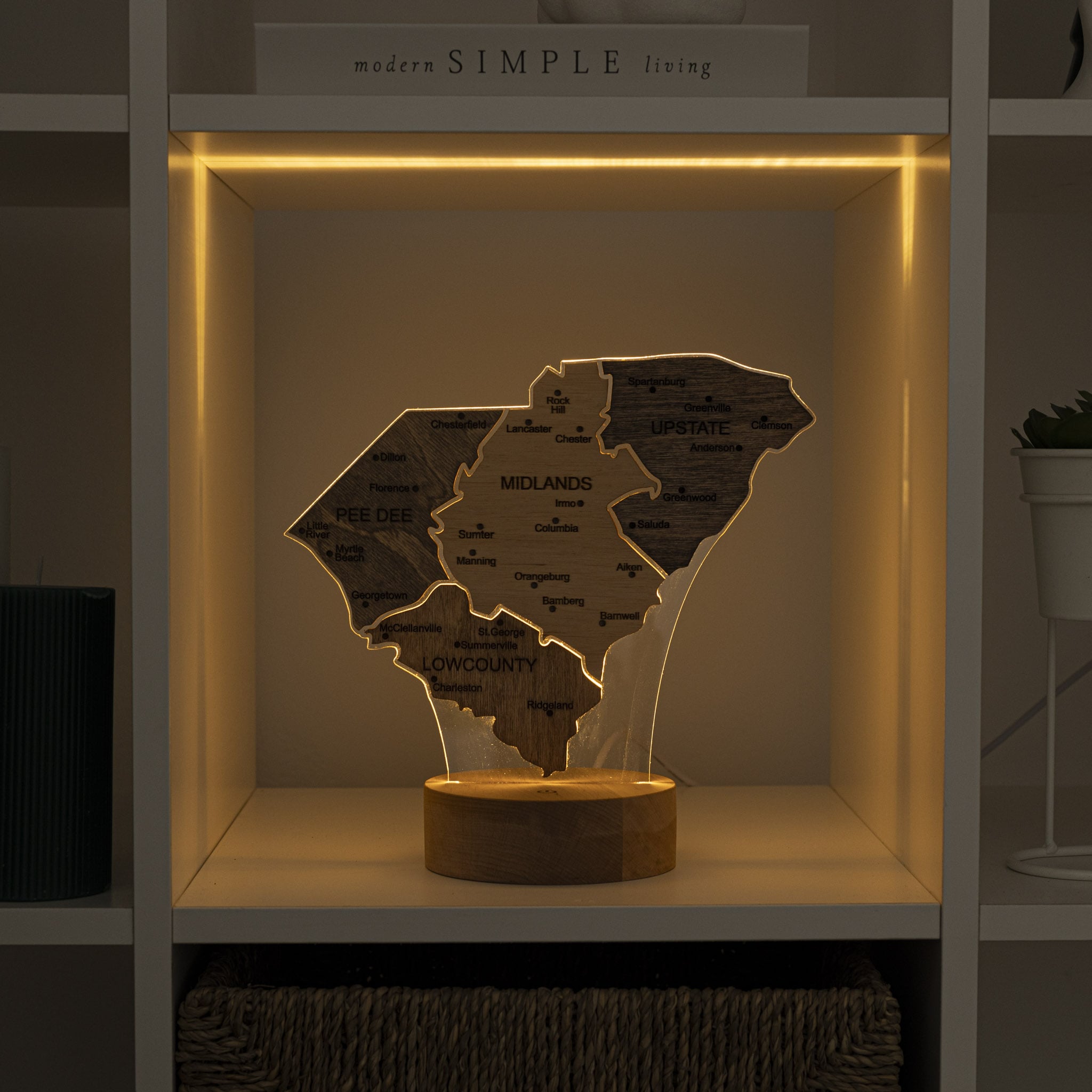 Wooden map of Wisconsin with engraved names, illuminated by a warm light on a shelf.