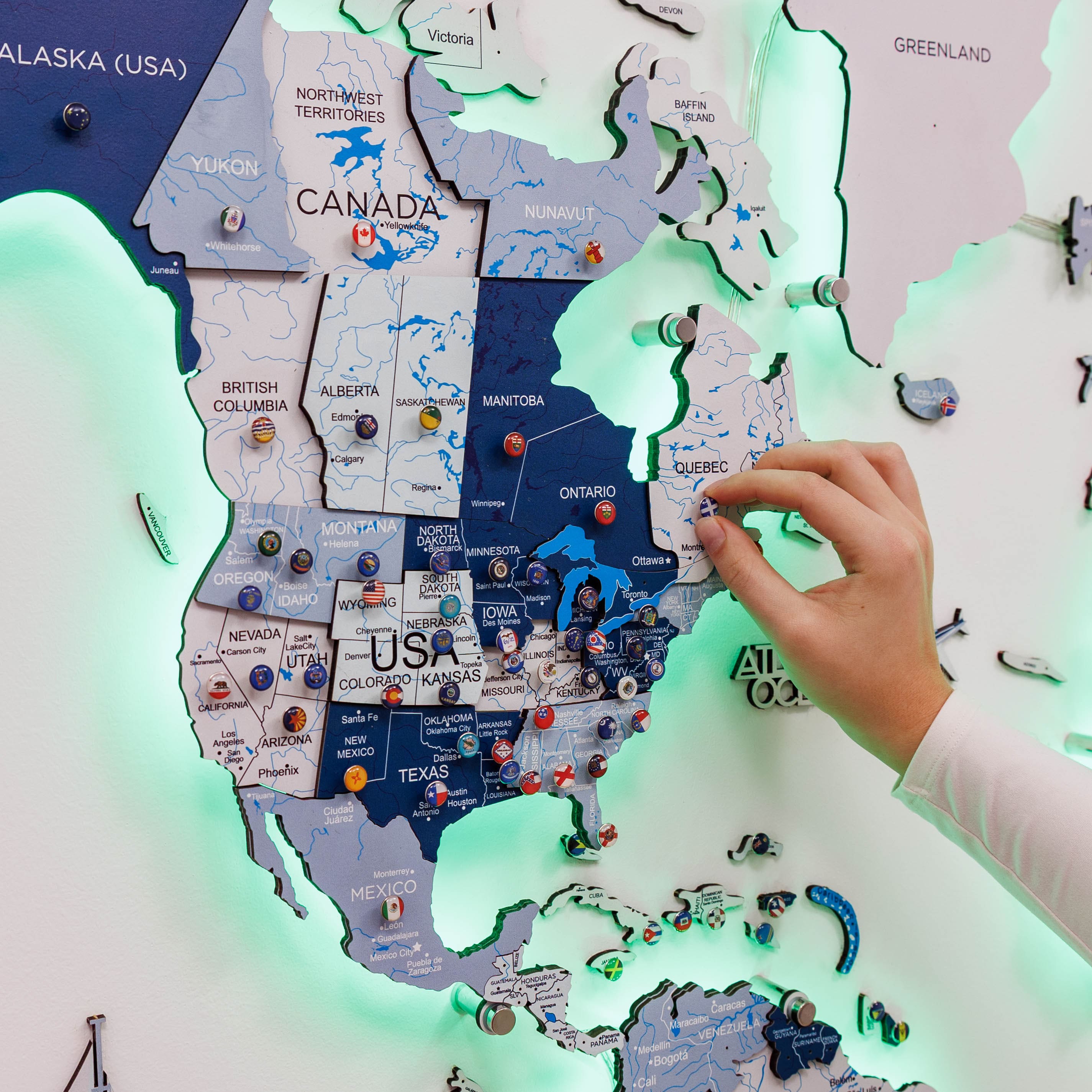Map of North America with pins and a hand interacting with it, illuminated by green light.
