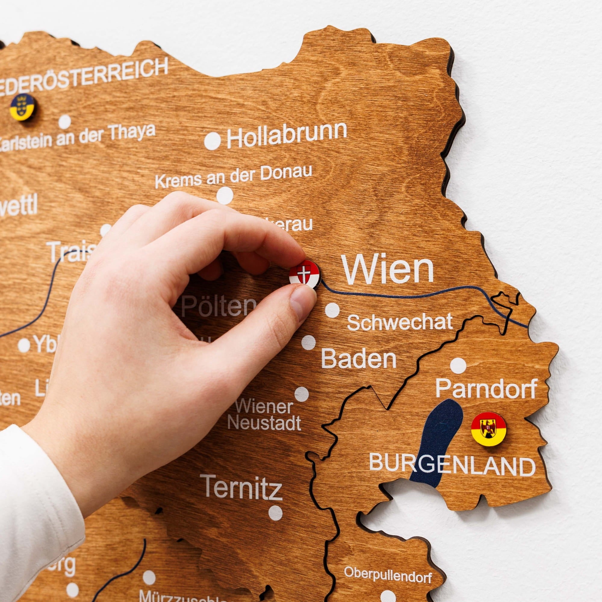 Hand placing a red pin on a wooden map of Austria, highlighting Vienna.