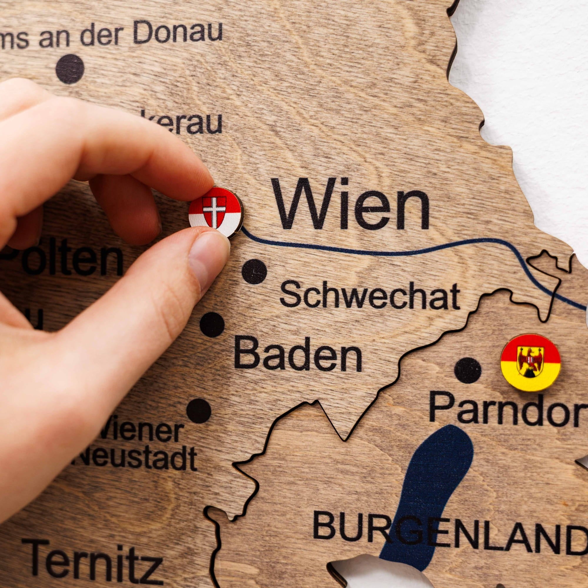 Wooden map of Austria with a hand placing a flag sticker on 'Wien'.