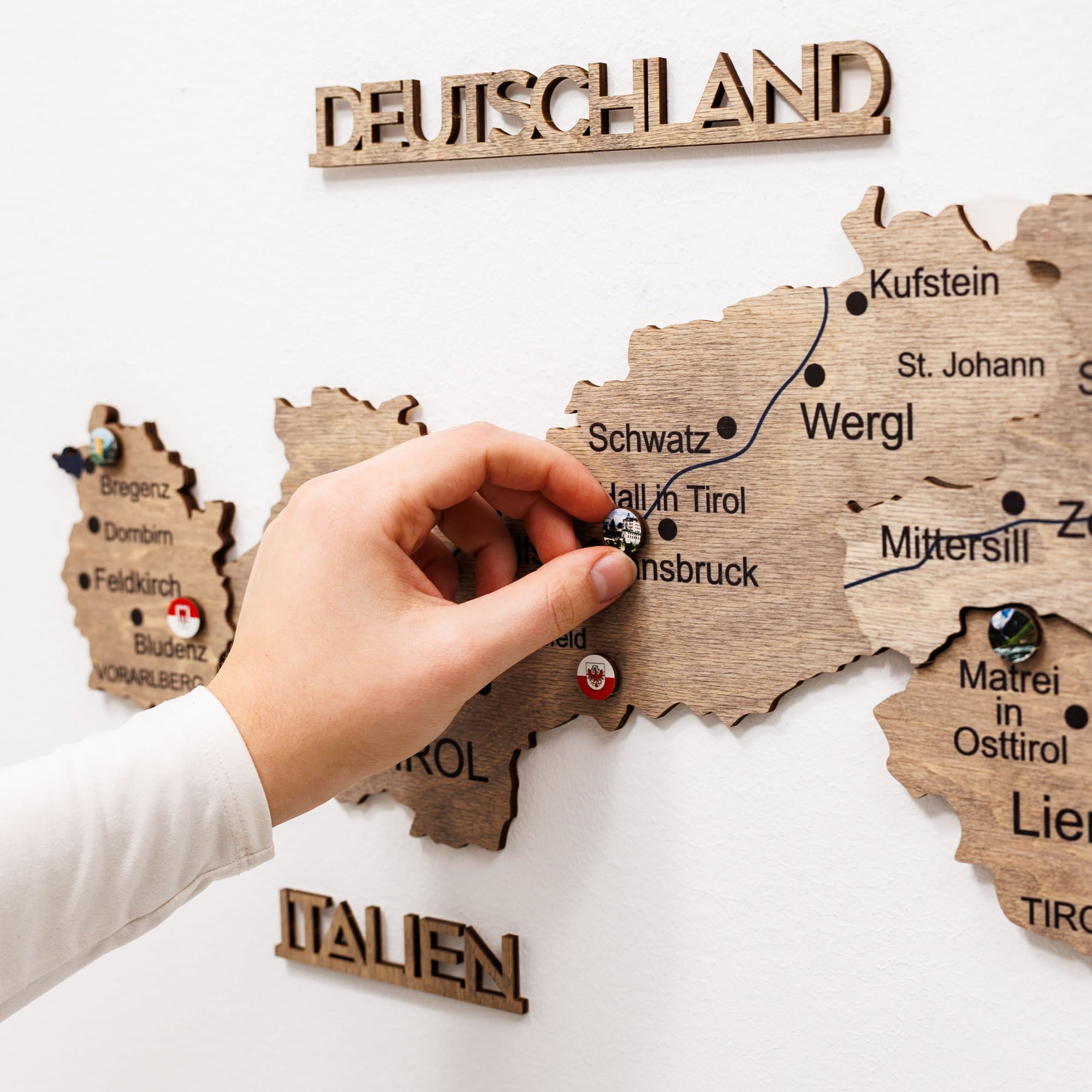 Wooden map of Germany with a hand placing a pin on a city.