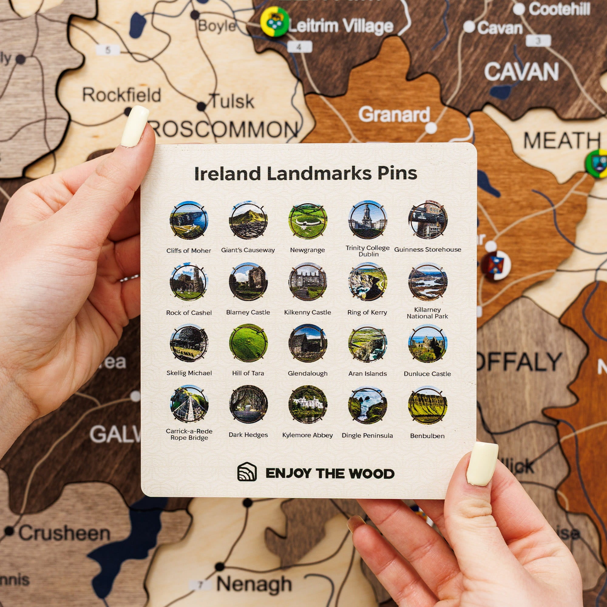 Sheet of Ireland landmarks pins held over a wooden map of Ireland.