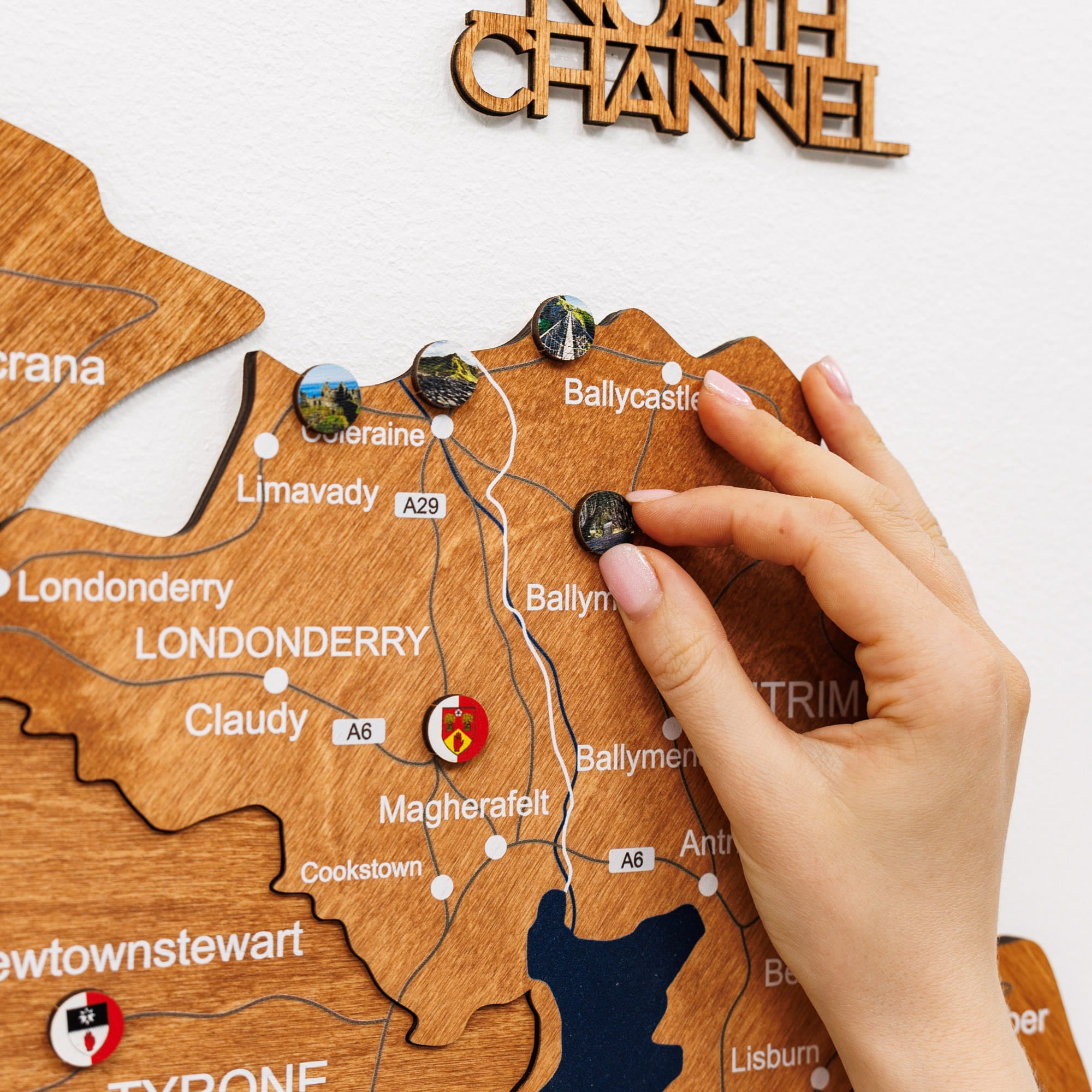 Wooden map of Northern Ireland with a hand placing a pin on Londonderry.