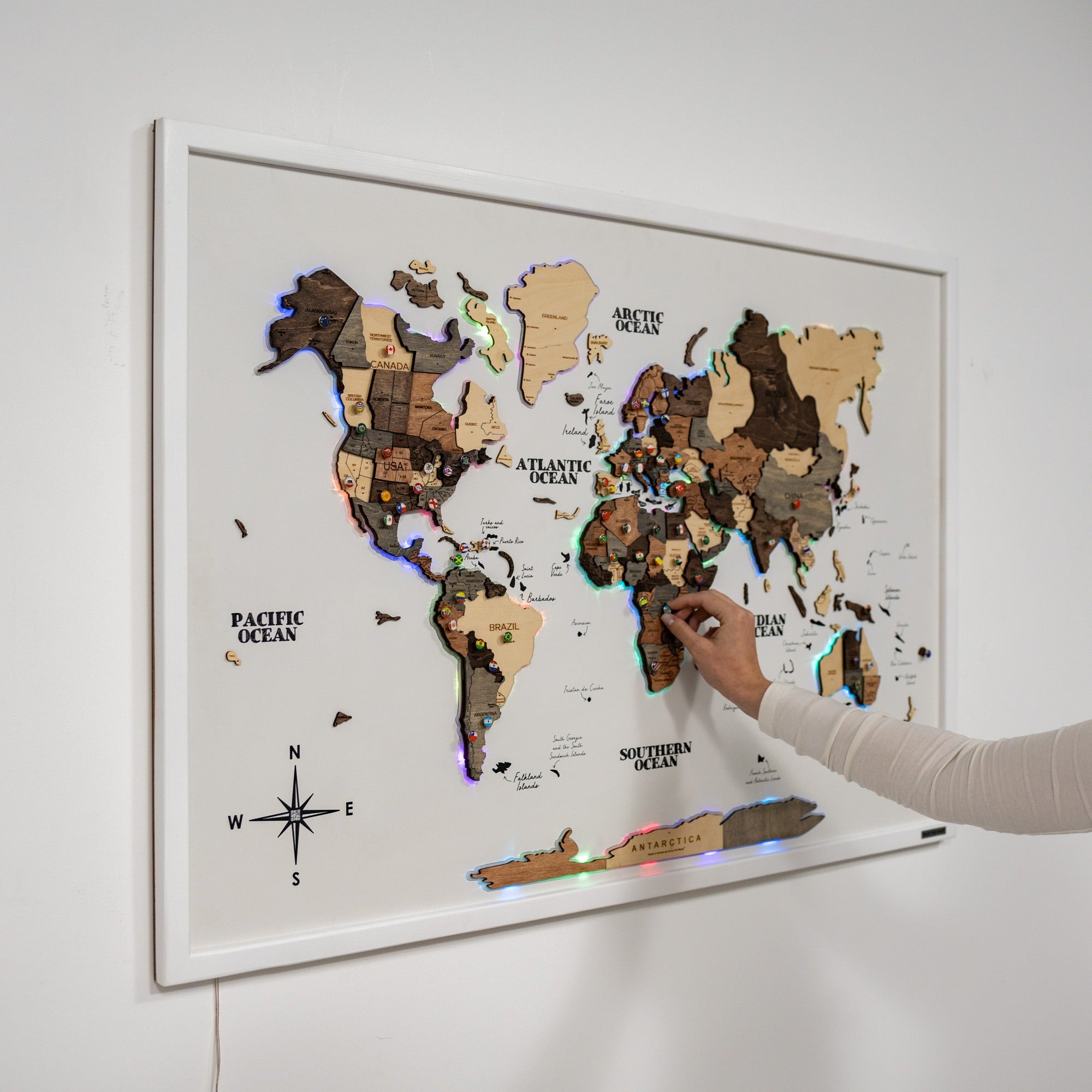 World map with LED lights on a white wall, being touched by a hand.