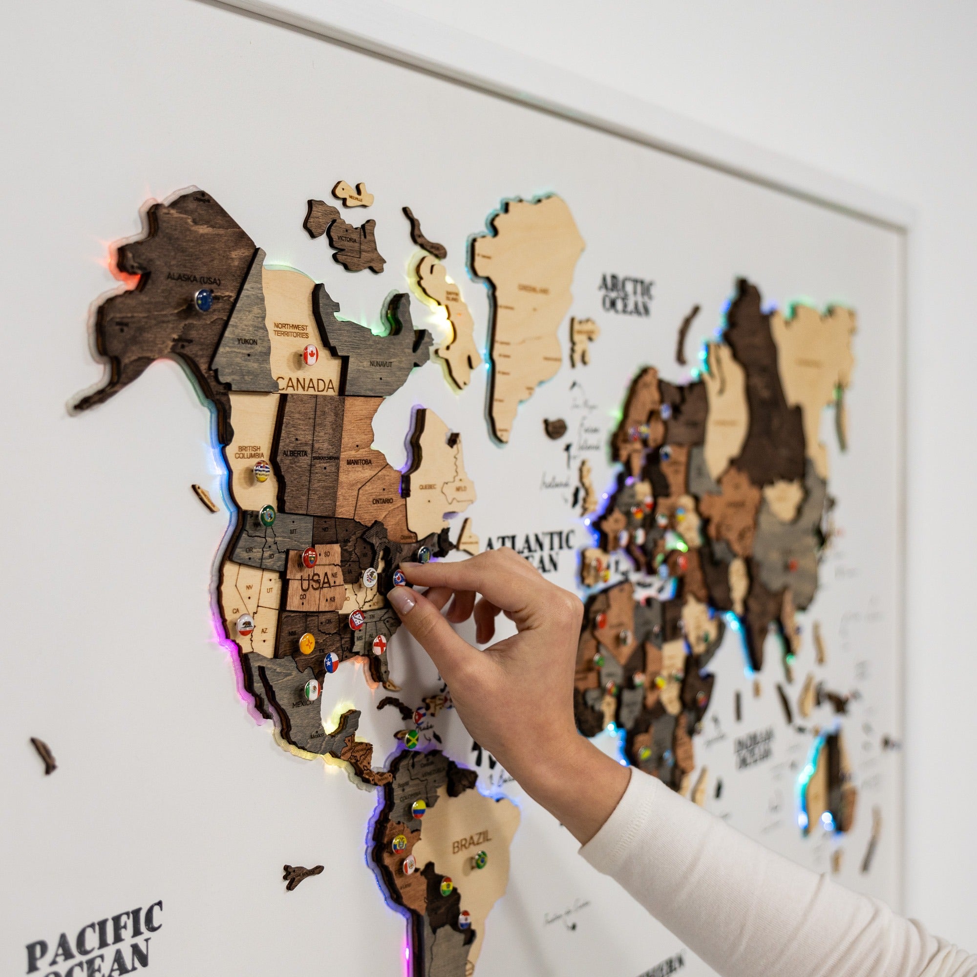 Wooden world map with LED lights, hand pointing at a country.