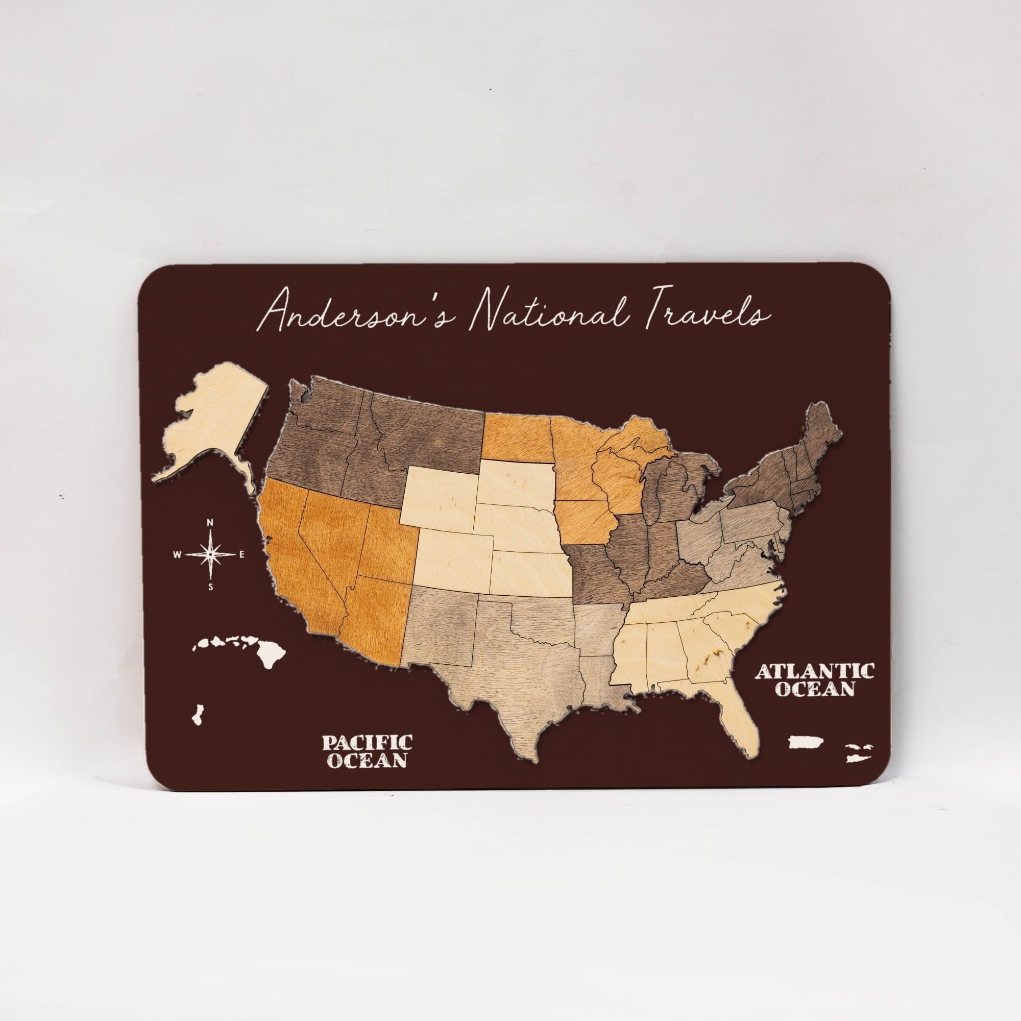 A rectangular dark brown map plaque featuring a stylized United States with states in different wood-tone shades, labeled 'Anderson's National Travel' and 'Pacific Ocean' and 'Atlantic Ocean,' photographed on a light neutral background.