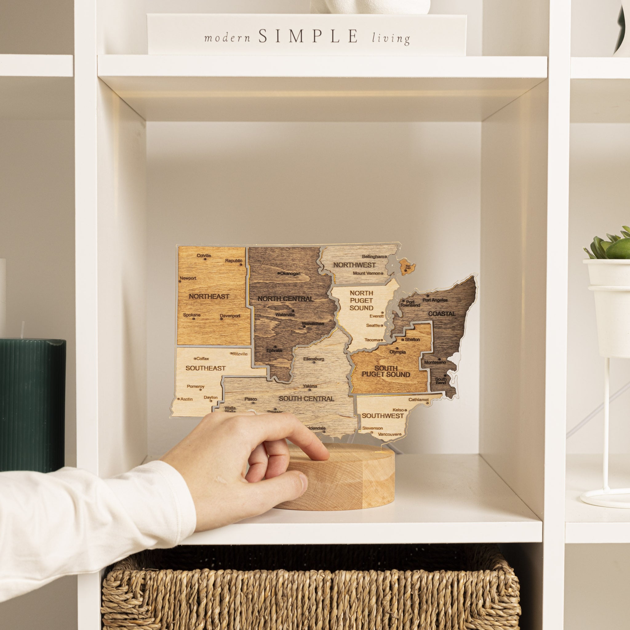 Wooden map of Washington state on a shelf with a hand reaching out to touch it.
