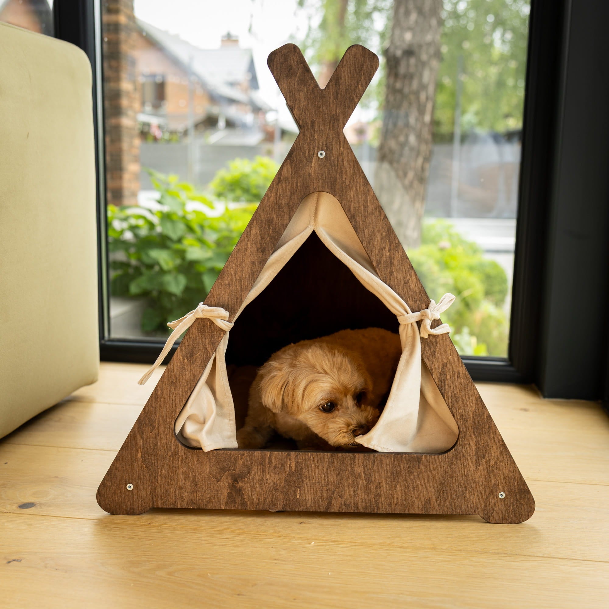 Wooden pet teepee with a dog peeking out on a wooden floor.