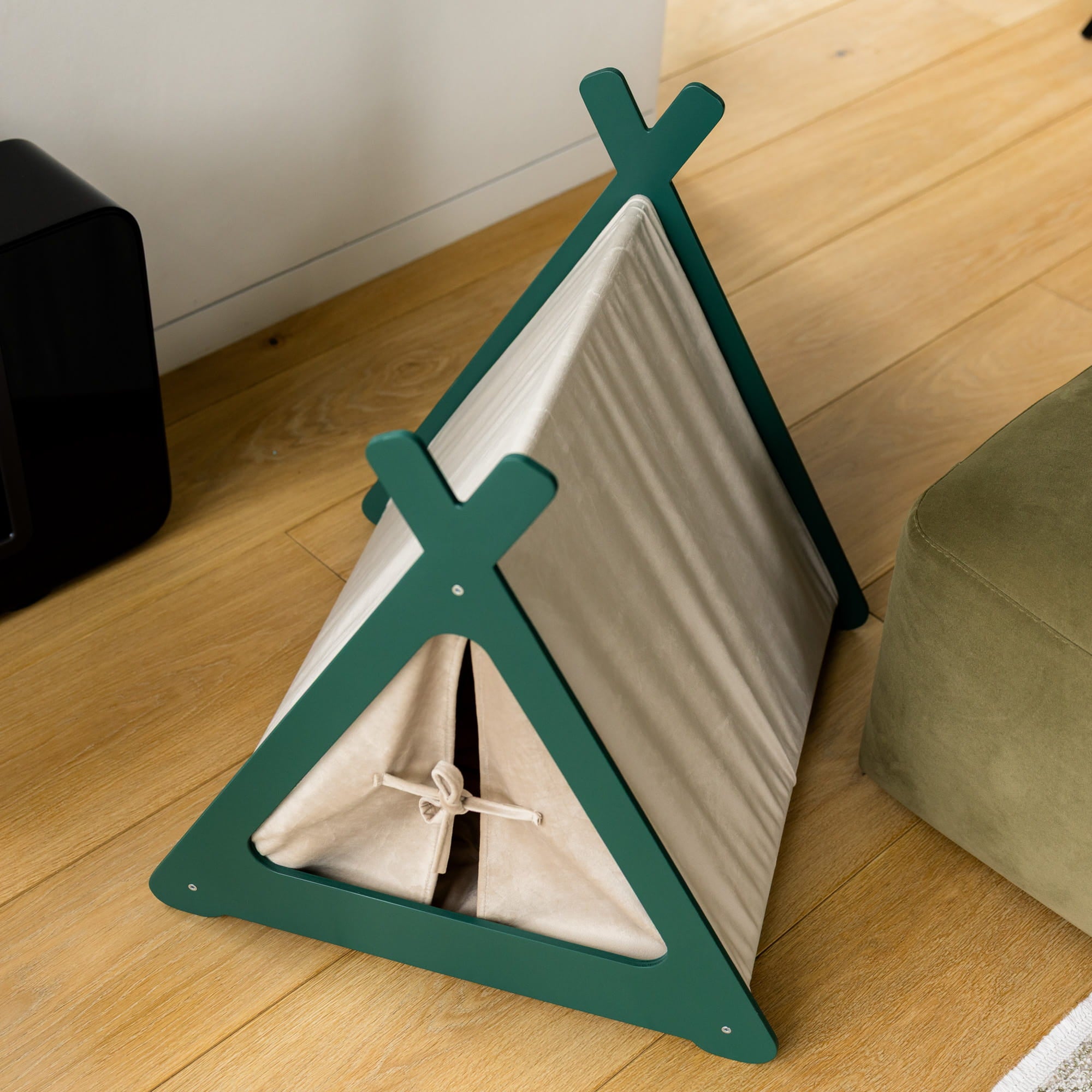 Green pet tent on a wooden floor with a white wall in the background