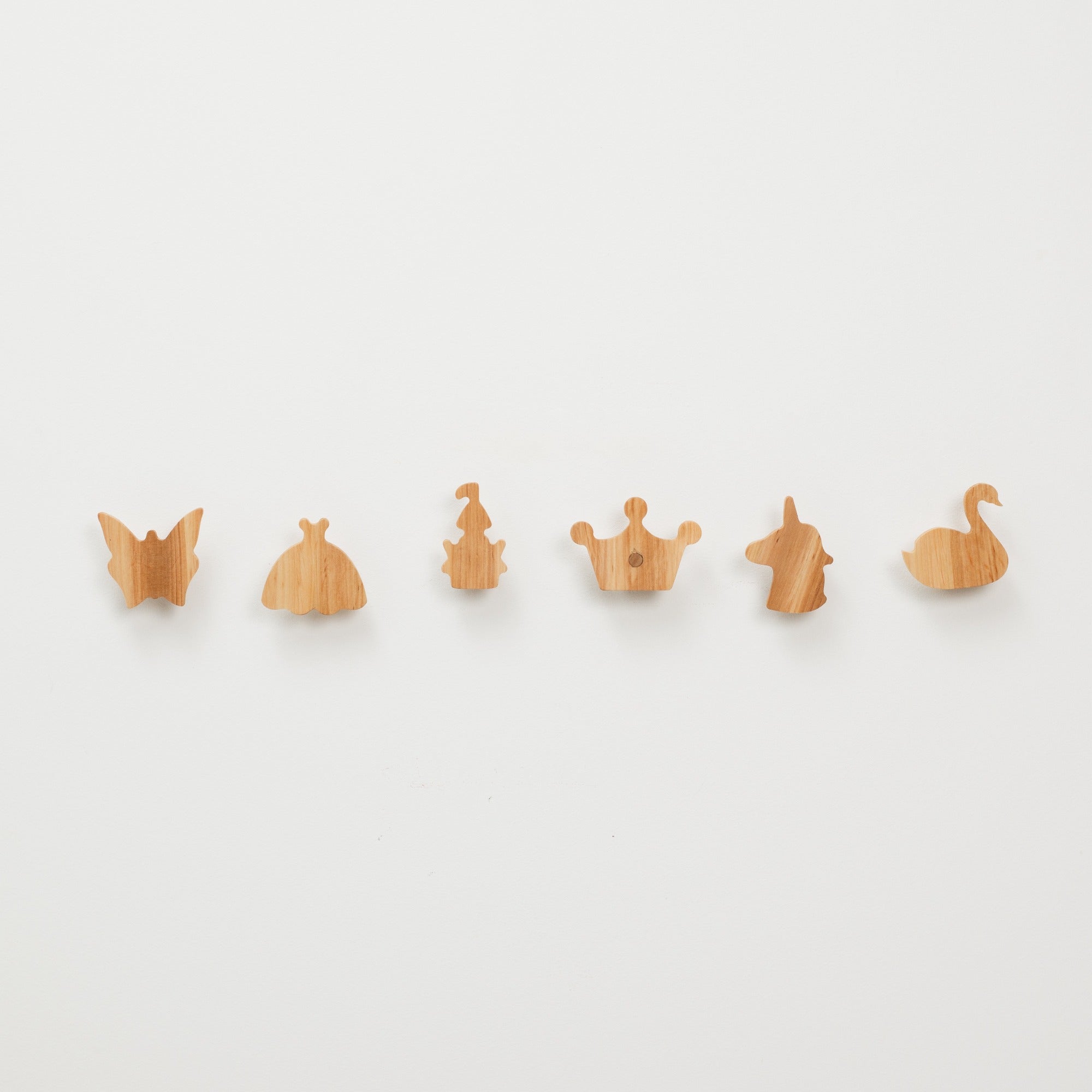 Set of wooden wall hooks shaped like butterflies, dresses, a crown, a unicorn, and a duck on a white background.