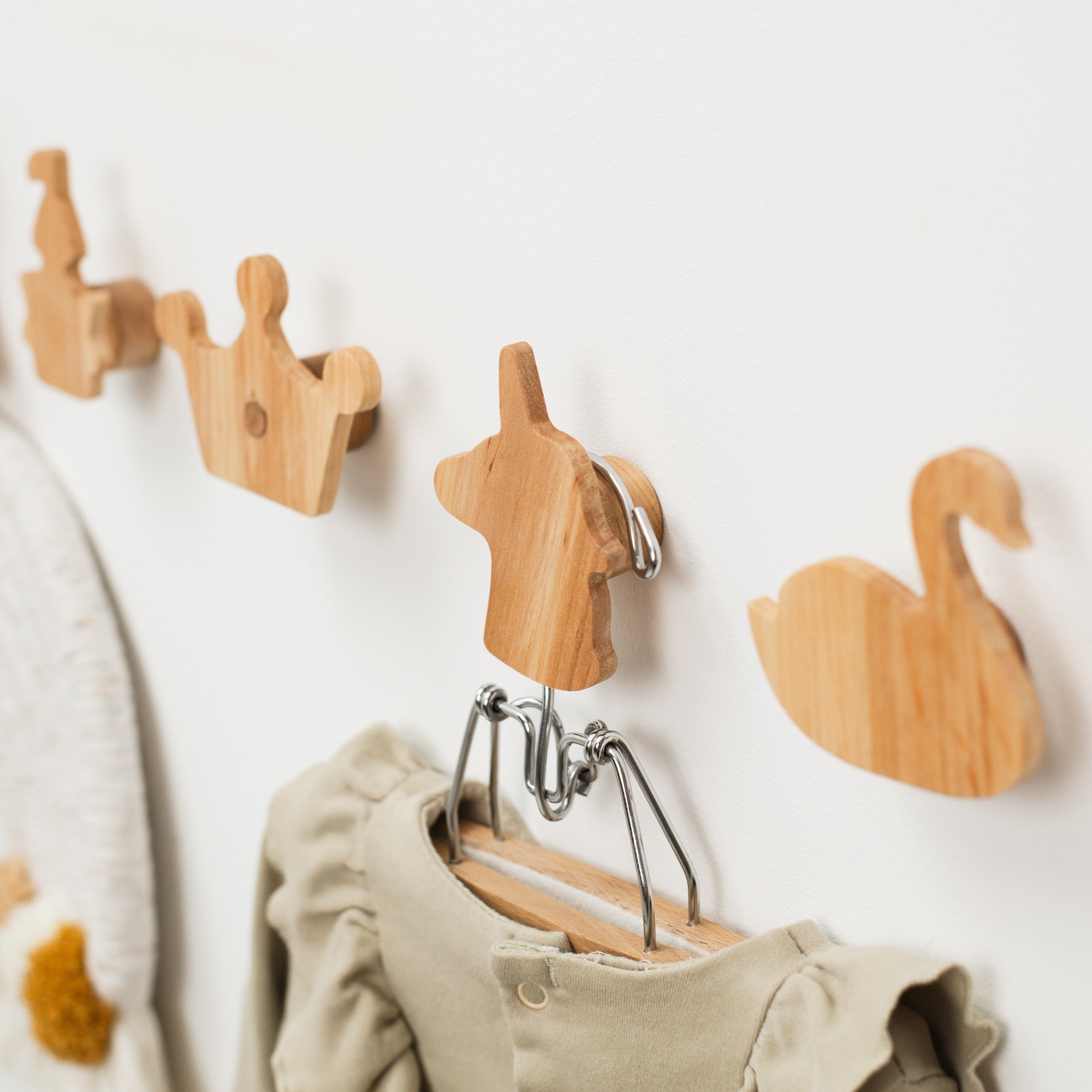 Wooden wall hooks shaped like a swan, heart, and crown on a white wall with a baby outfit hanging from one of them.