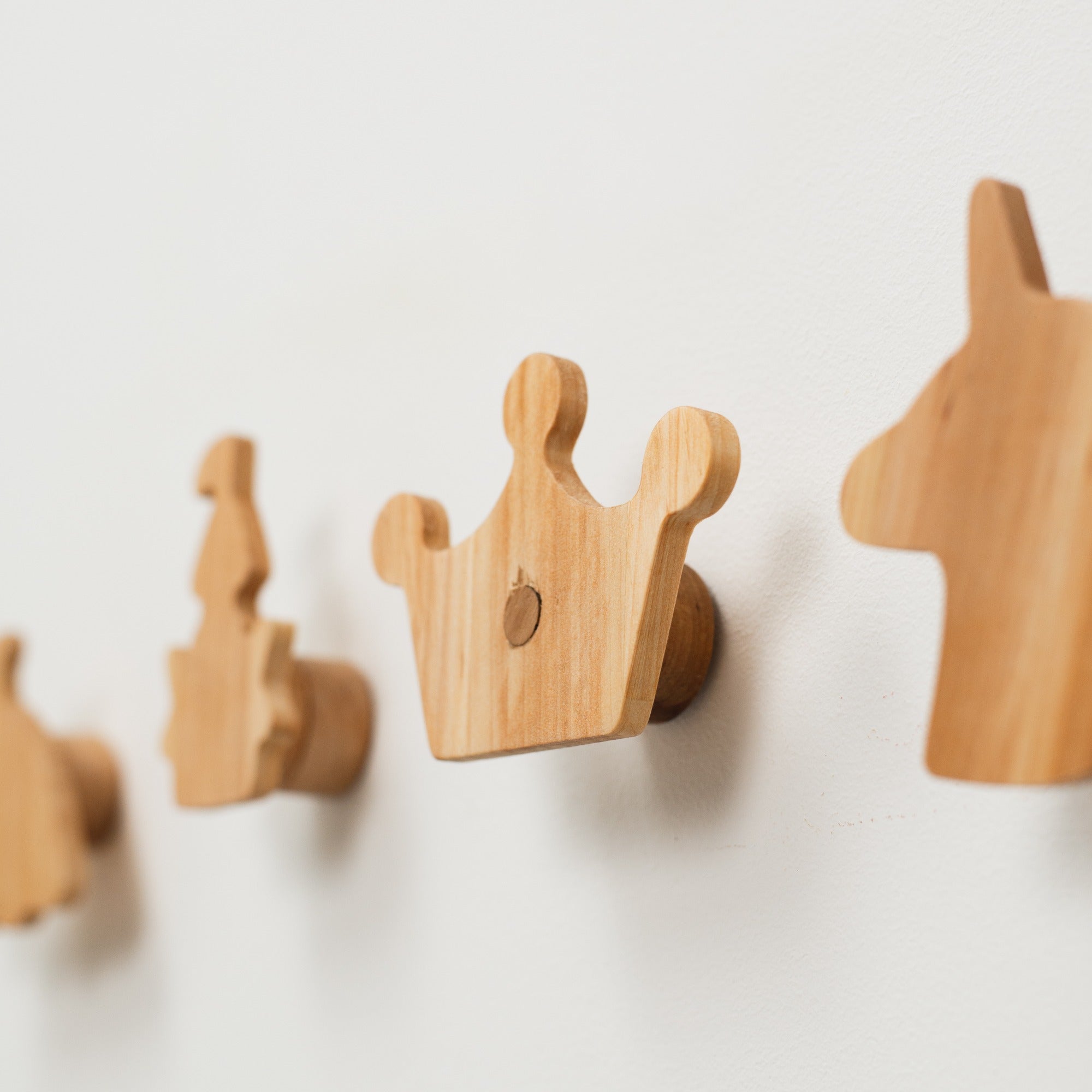 Wooden wall hooks shaped like a crown, a lion, and a castle on a light background