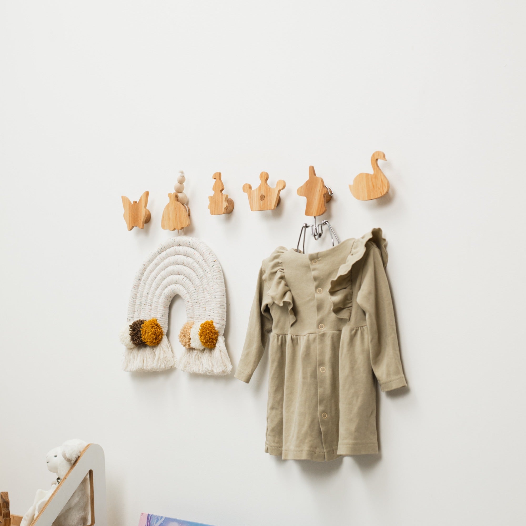 Wooden hooks on a white wall with a beige dress and decorative items.
