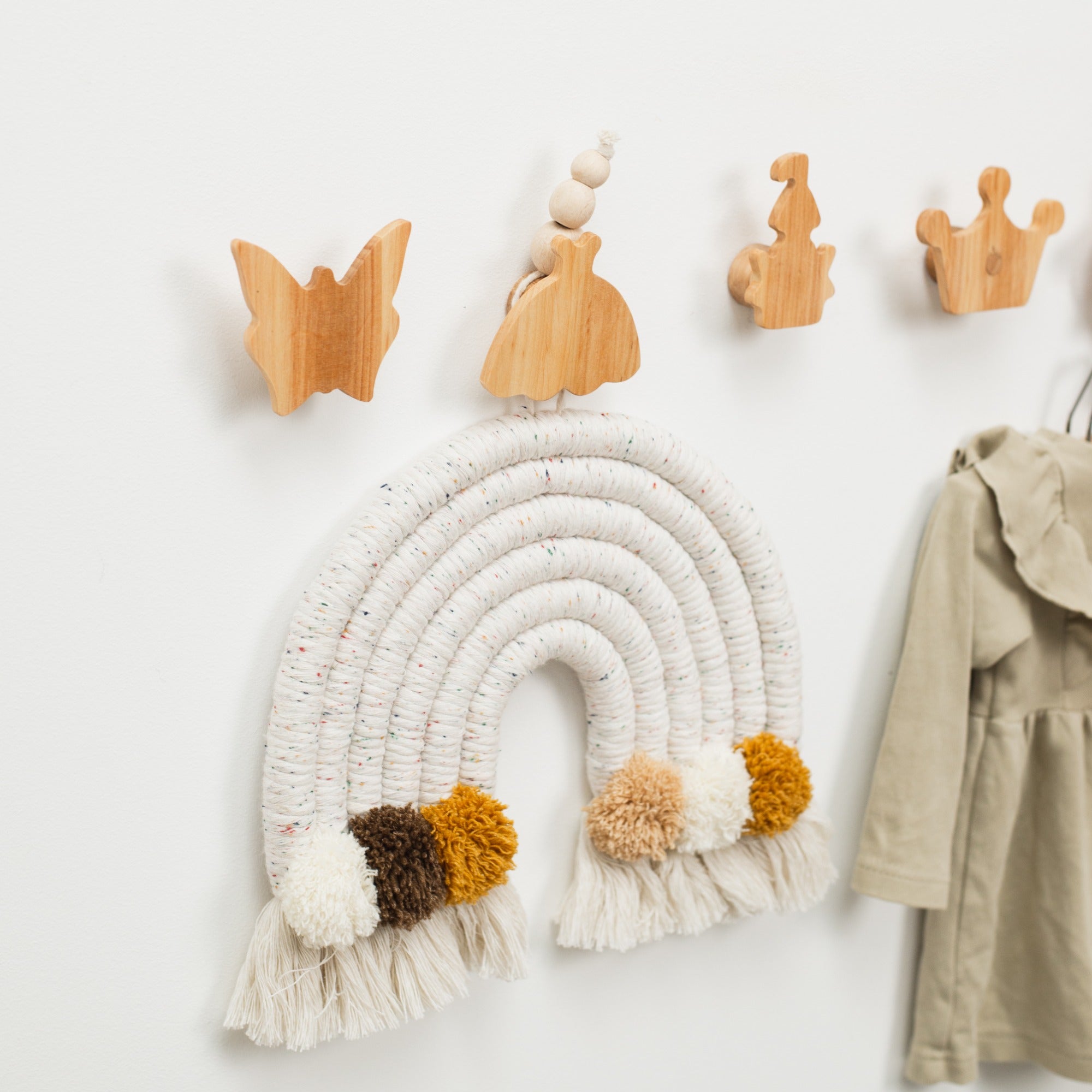 Wooden wall hooks and a decorative rainbow wall hanging on a white wall.