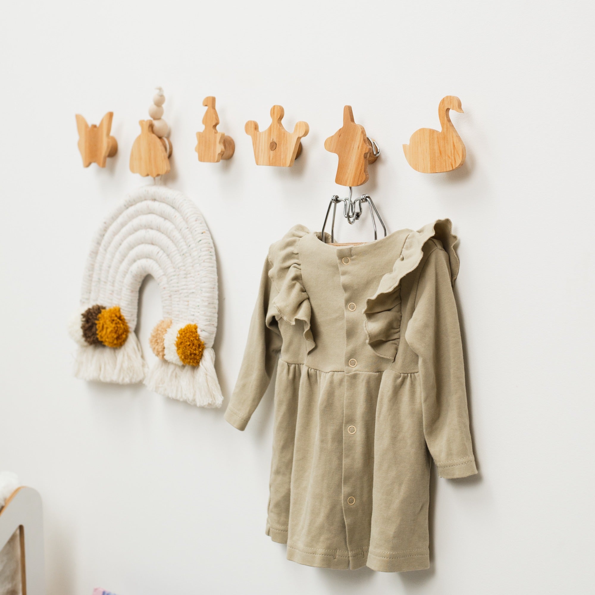 Wooden wall hooks with various shapes and a beige dress hanging on them against a white wall.