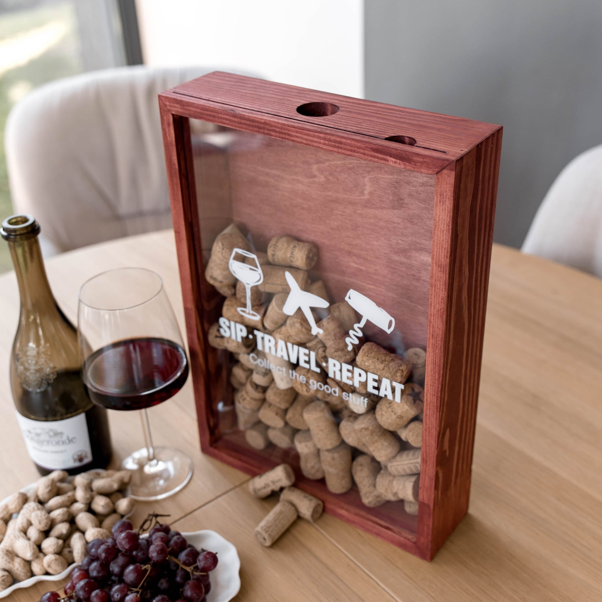 A wooden wine cork storage box with a clear front panel sits on a dining table.