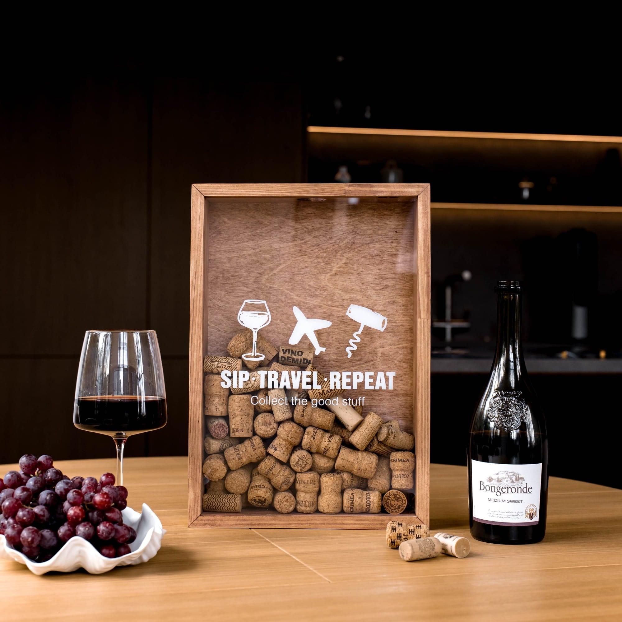 A wooden framed wine-themed wall art piece displayed on a wooden table