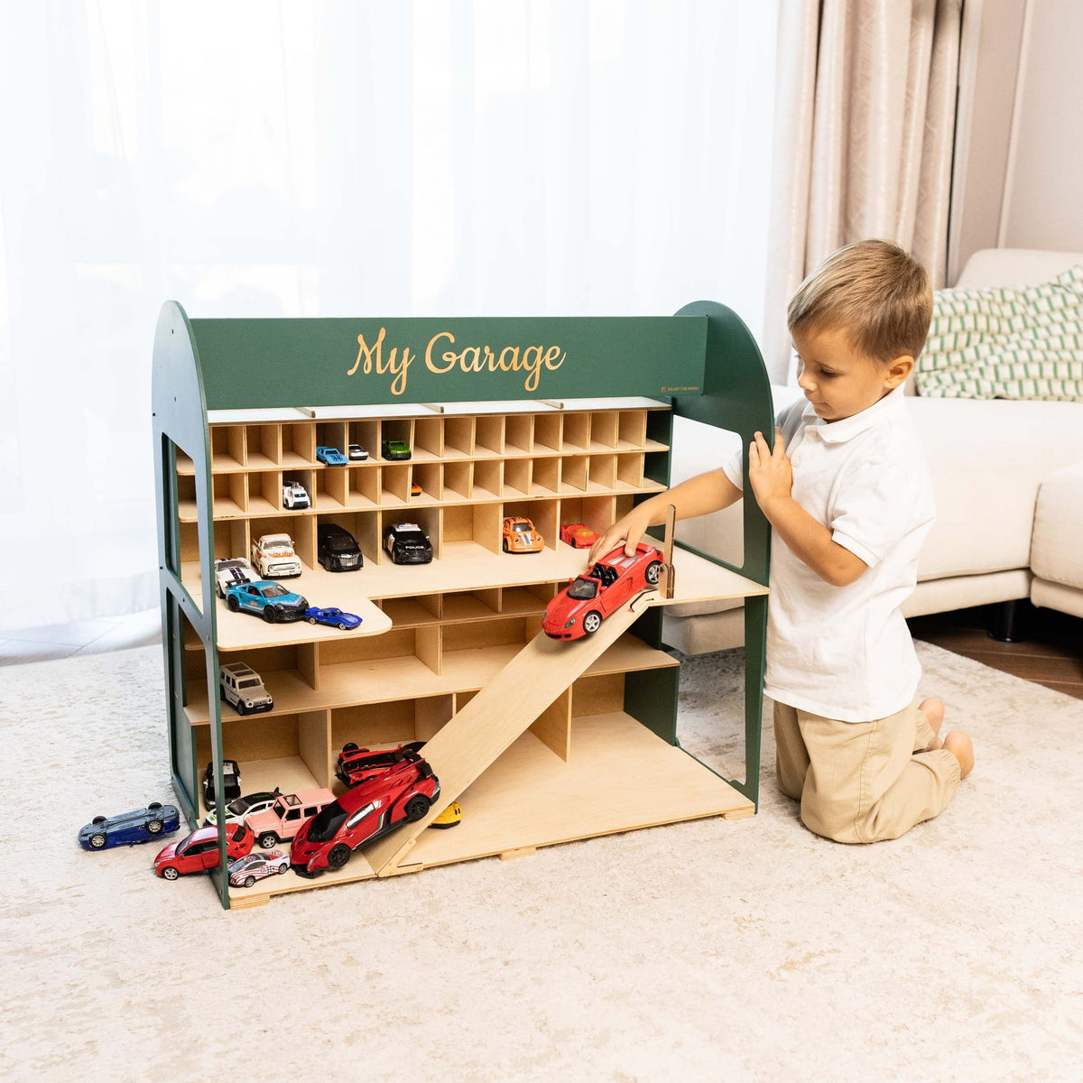The garage has a dark green exterior, a light wood interior, a ramp, and multiple toy cars.