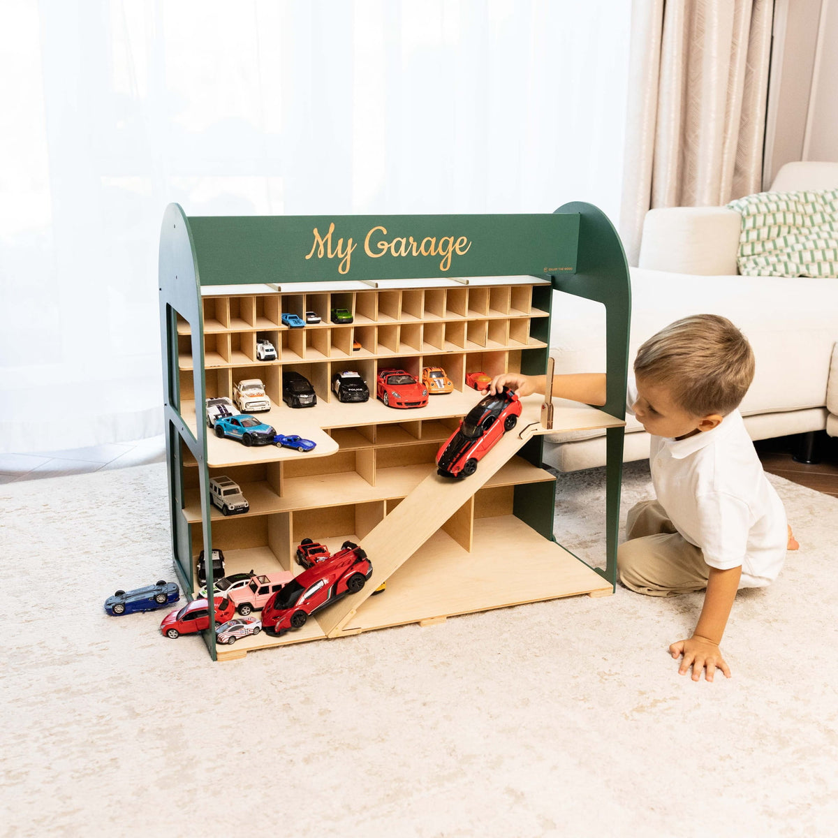  A young child is kneeling on the carpet next to the garage in a bright living room setting.