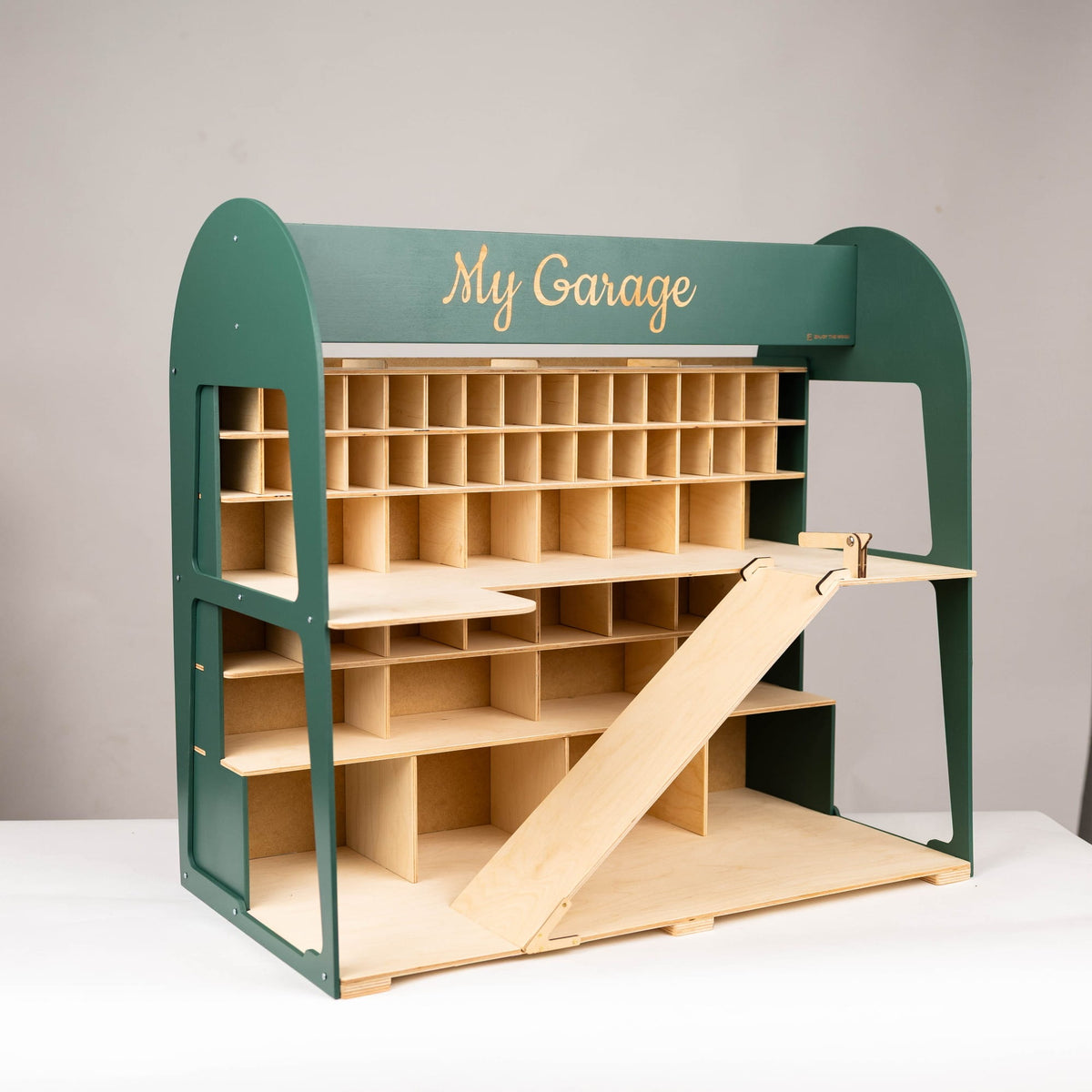 A wooden garage organizer with a dark green frame and light natural wood shelves, bins, and a ramp, featuring the words 'My Garage' in gold script on the top front.