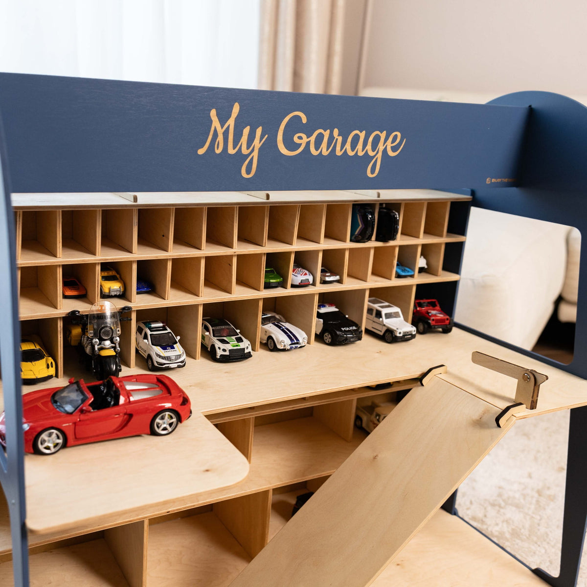 The garage is navy blue on the exterior with natural light wood shelves and ramps, and is decorated with small toy cars.
