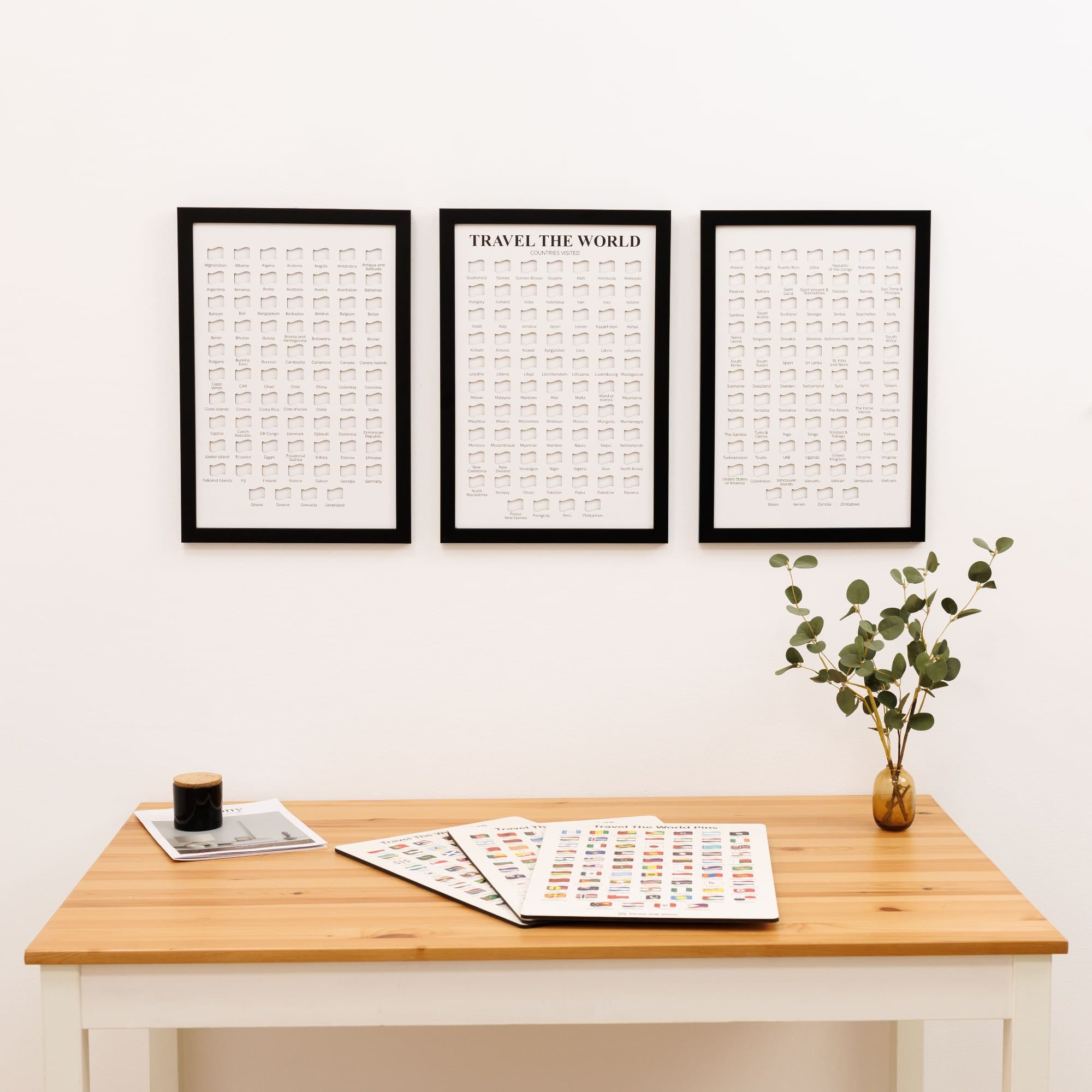 Three framed prints on a wall above a wooden desk with a plant and coffee cup.