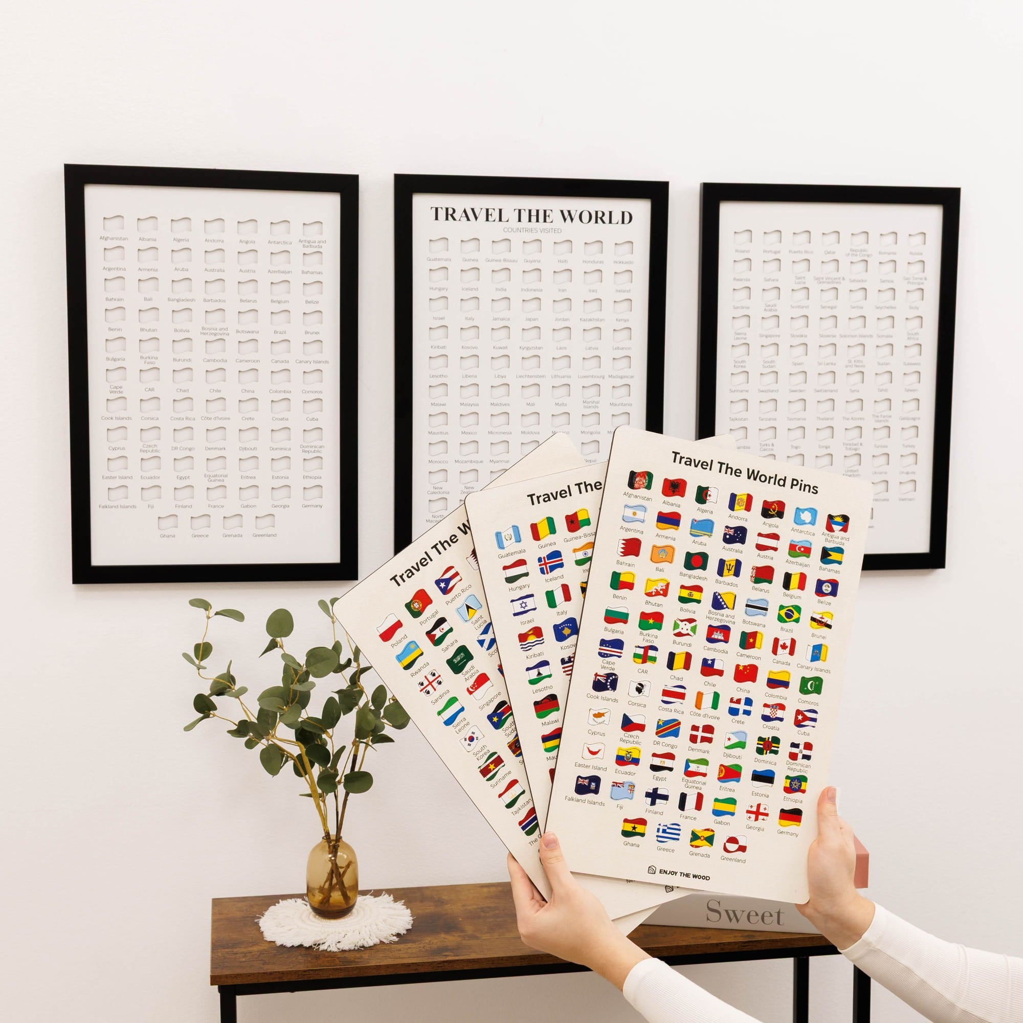Two hands holding a set of flag stickers with framed posters in the background.