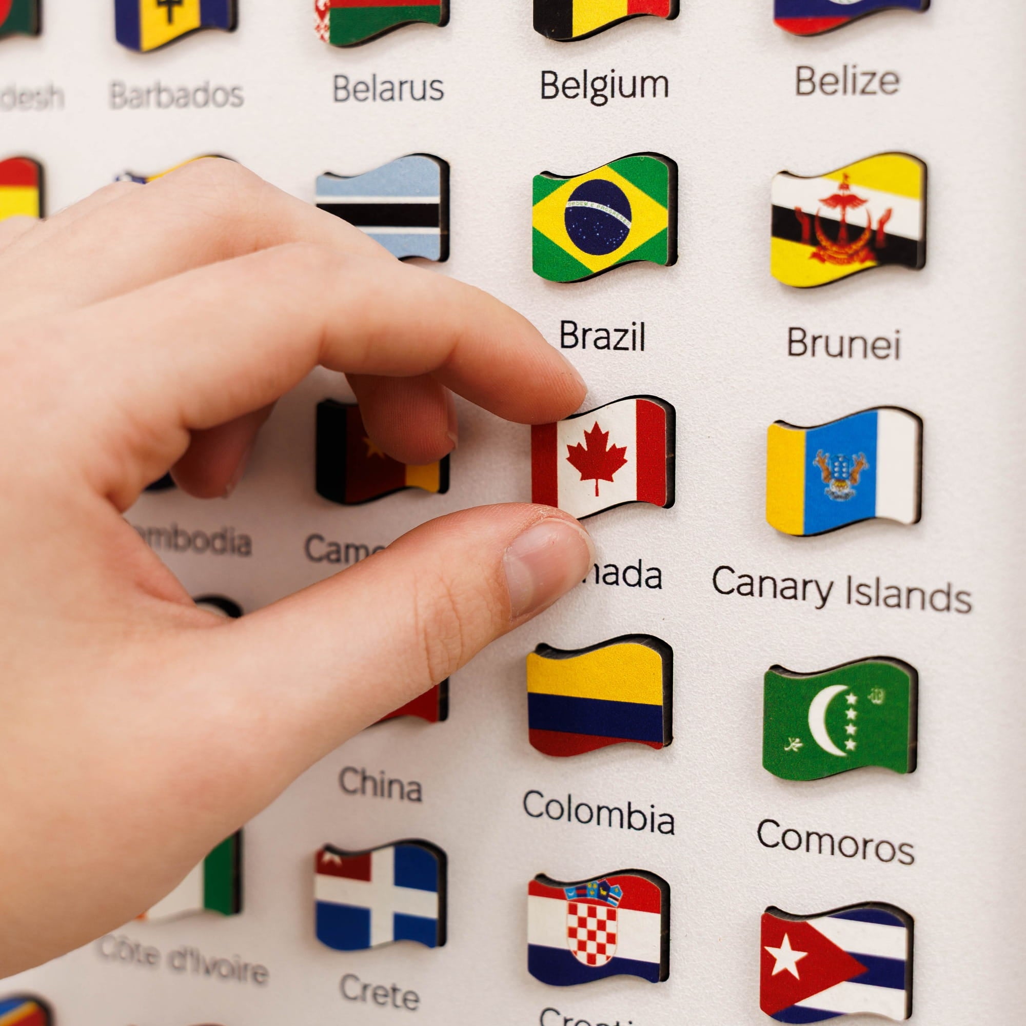Hand pressing a button with a Canadian flag on a board with various country flags.