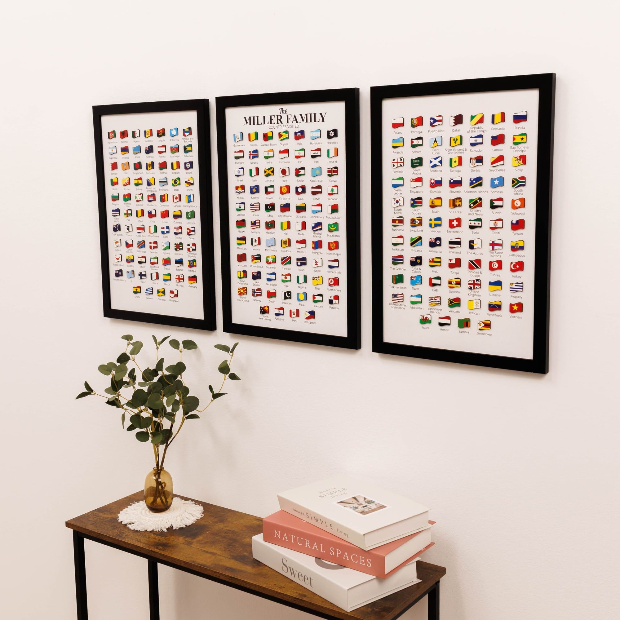 Three framed prints of world flags on a wall above a wooden console table with books and a plant.