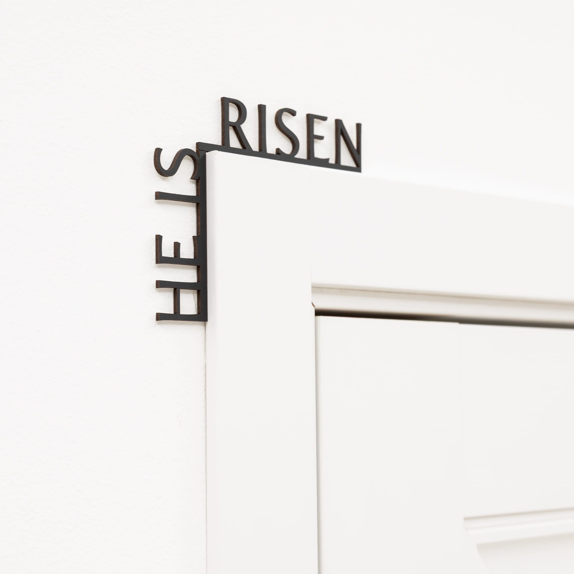 Decorative metal sign with 'HE IS RISEN' text on a white background