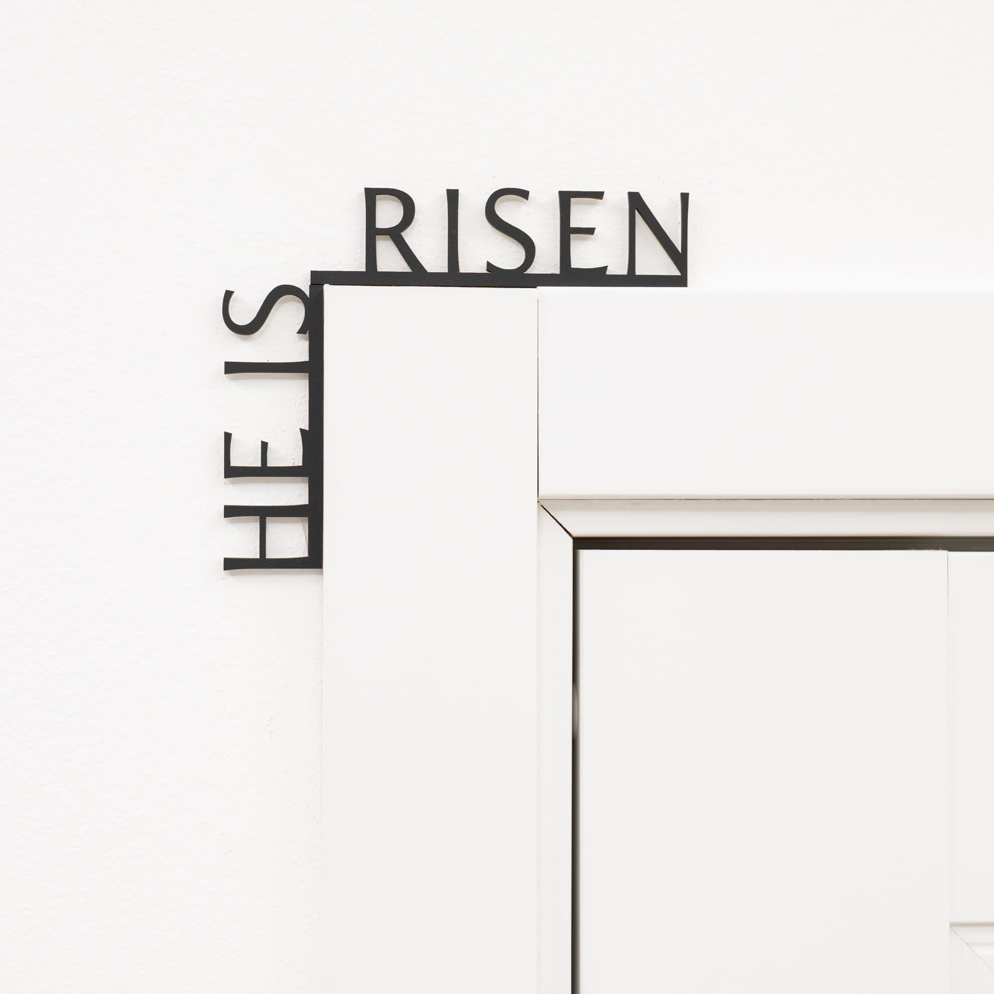 Decorative metal wall art with 'HE IS RISEN' text on a white background