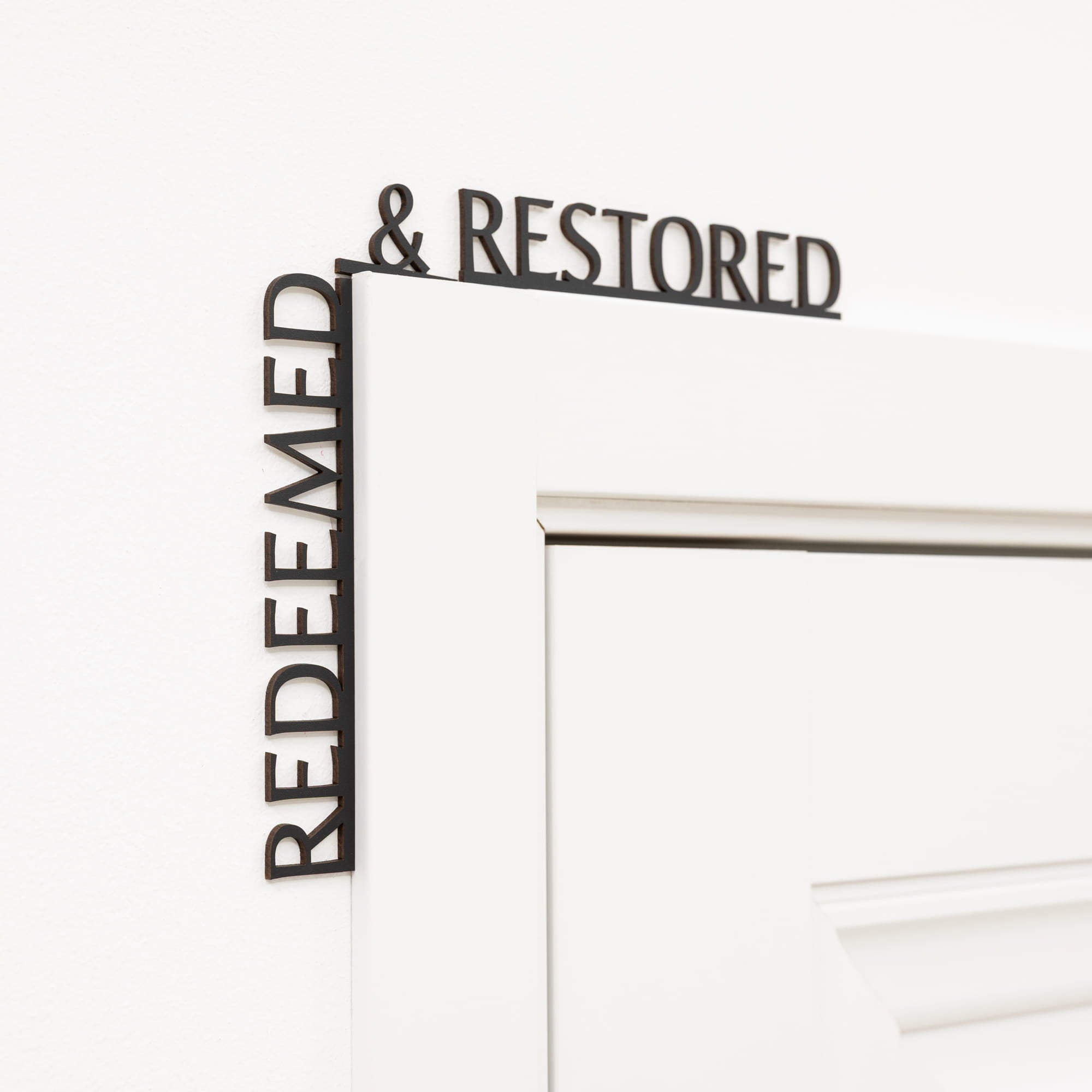 Decorative metal wall art with 'REDEEMED & RESTORED' text on a white background