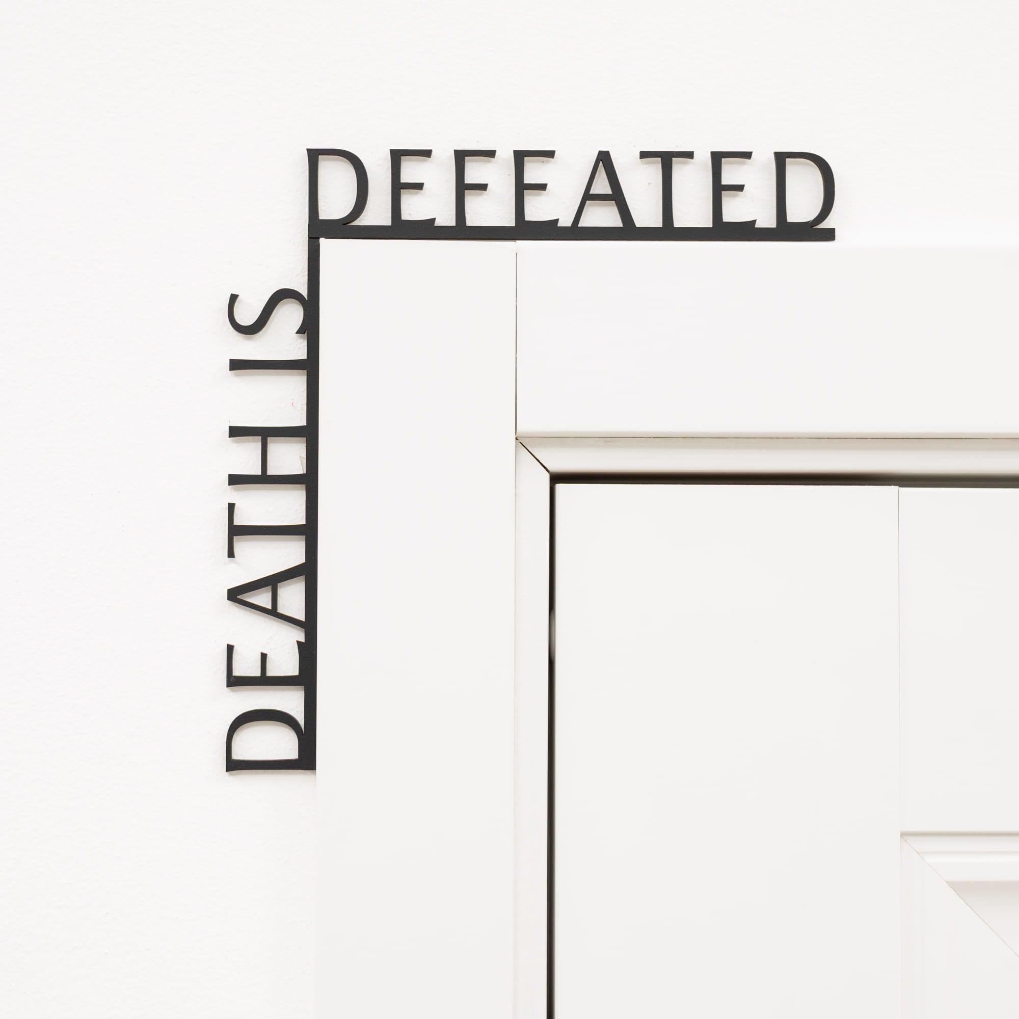 Decorative wall art with 'DEFEATED' and 'DEATH IS' text on a white background
