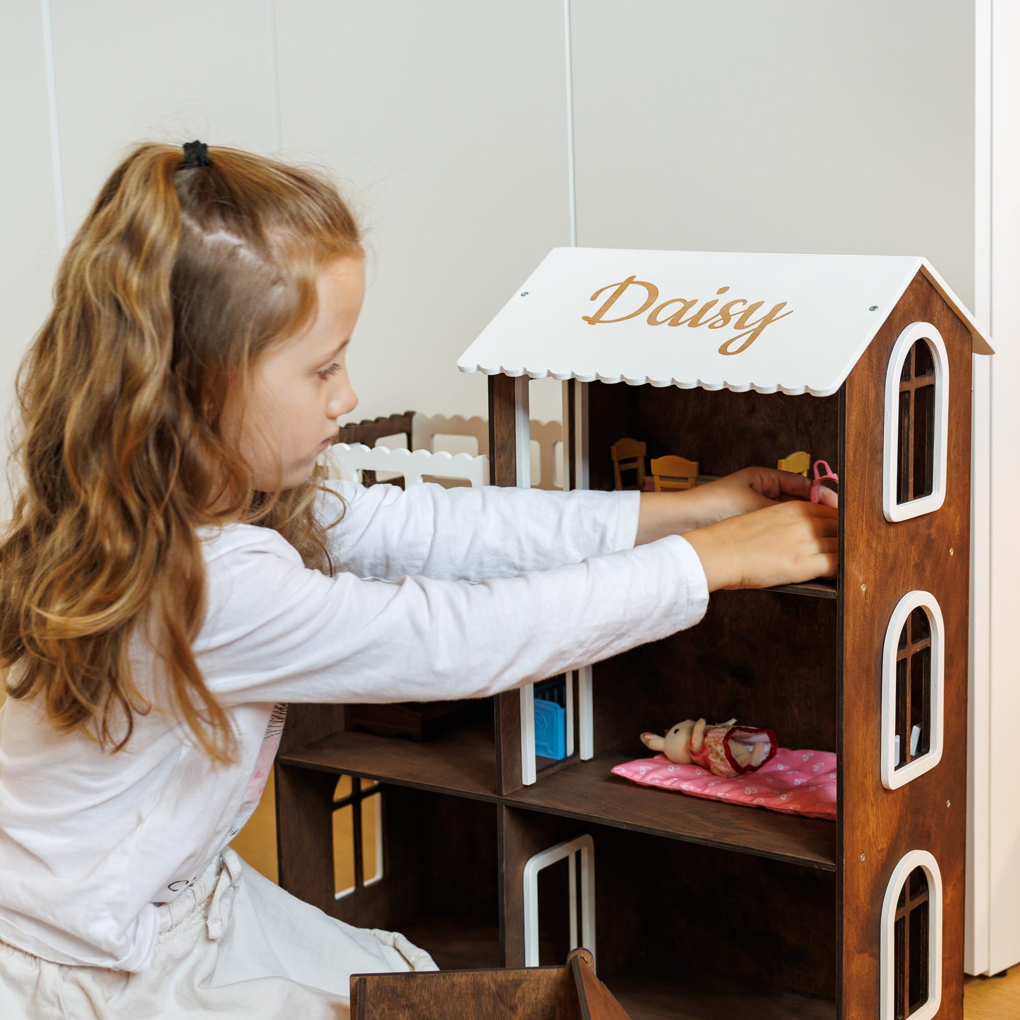 The dollhouse is dark brown wood with white-trimmed window 