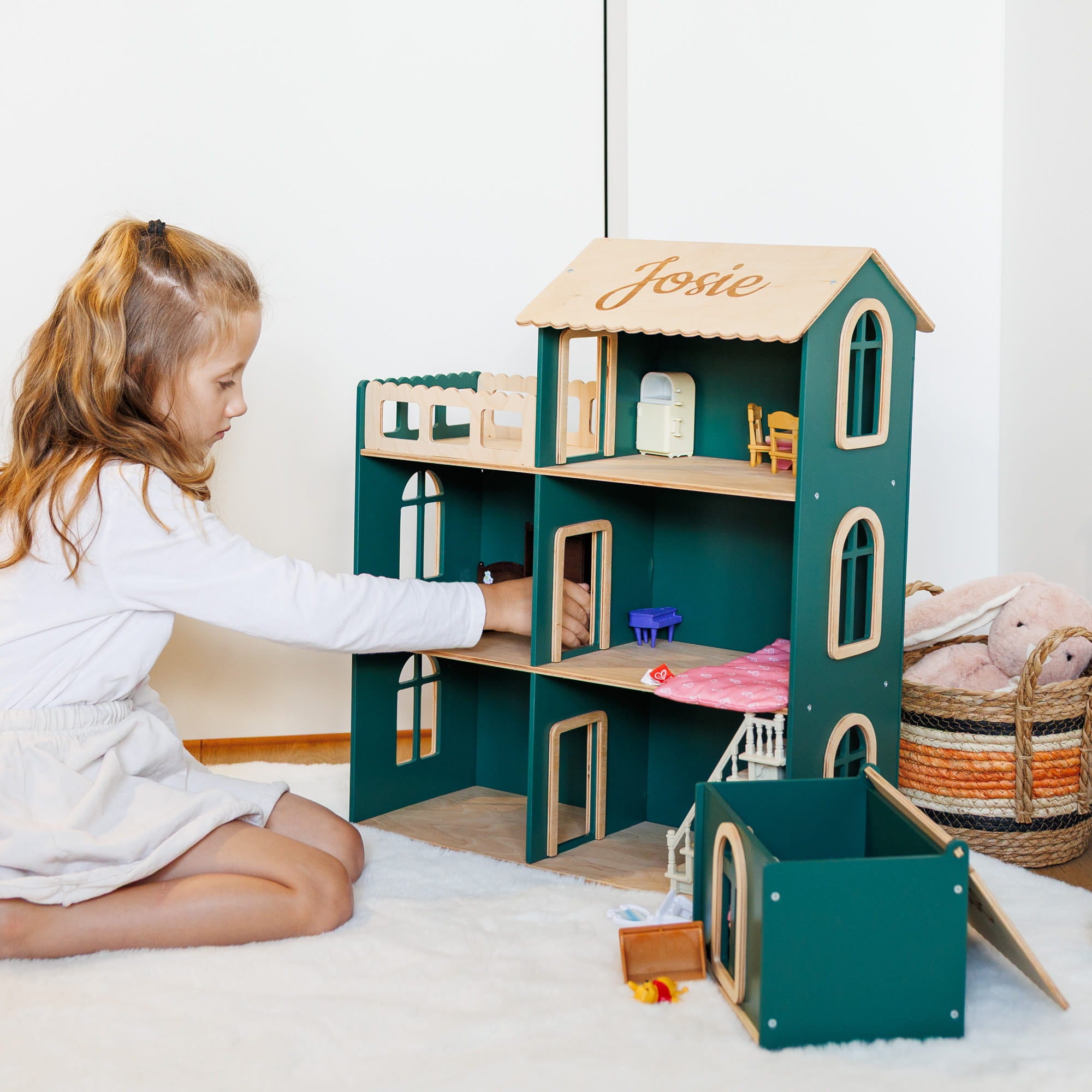 The dollhouse is dark teal green with light wood paneling and the name 'Josie' written on the roof.