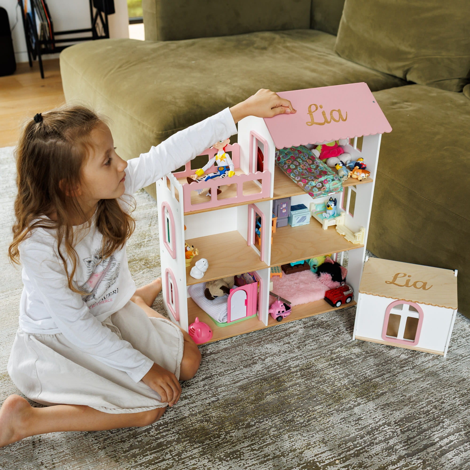 The dollhouse is decorated with small furniture pieces and toys, and a matching small dollhouse window piece sits beside it.